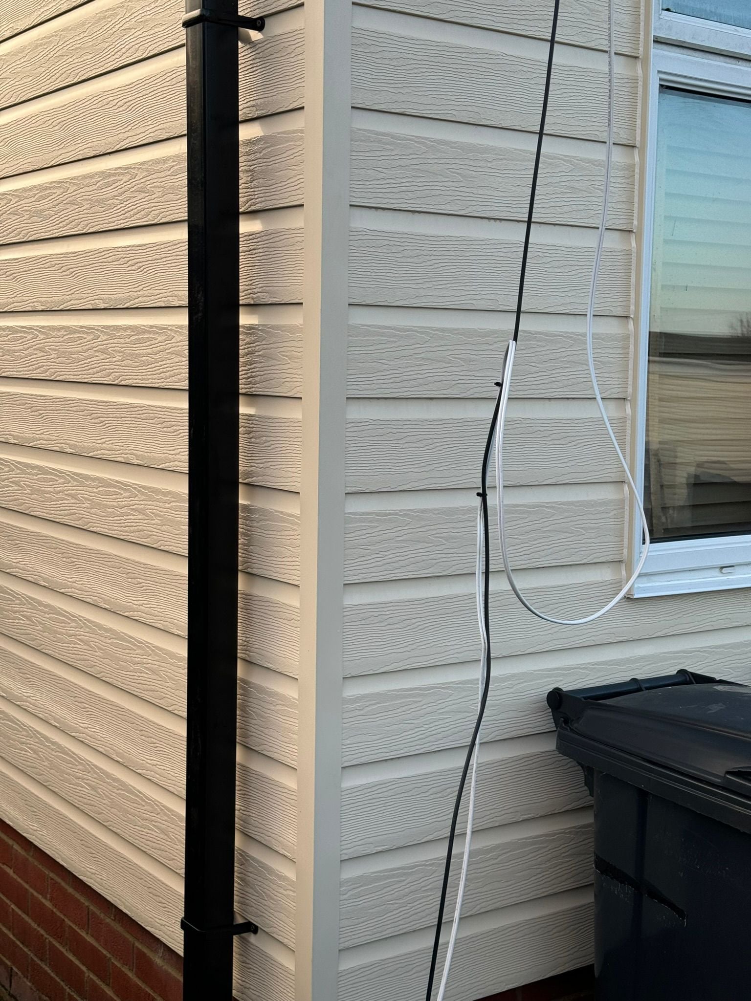 Close-up detail of new cream cladding corner with black downpipe and guttering