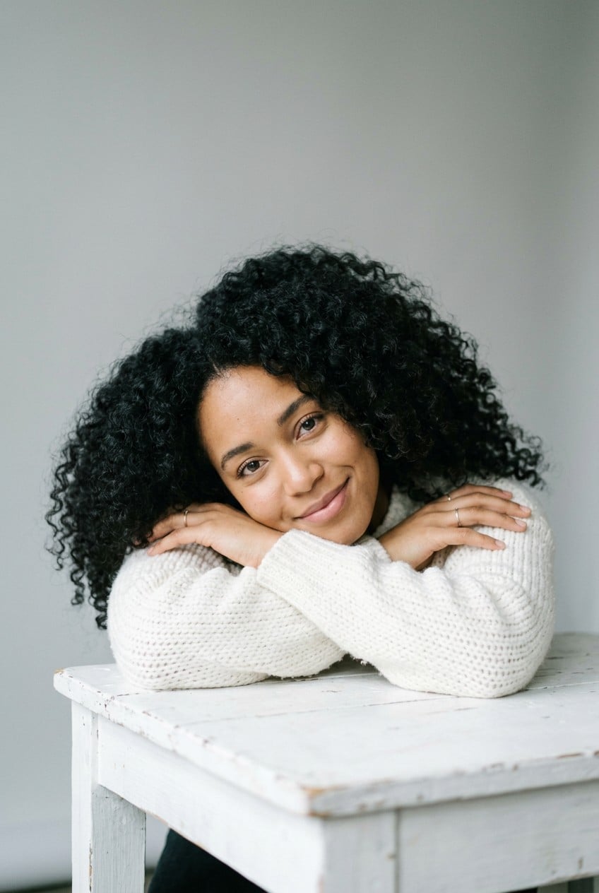 Smiling woman in a white knit sweater resting her head on her arms