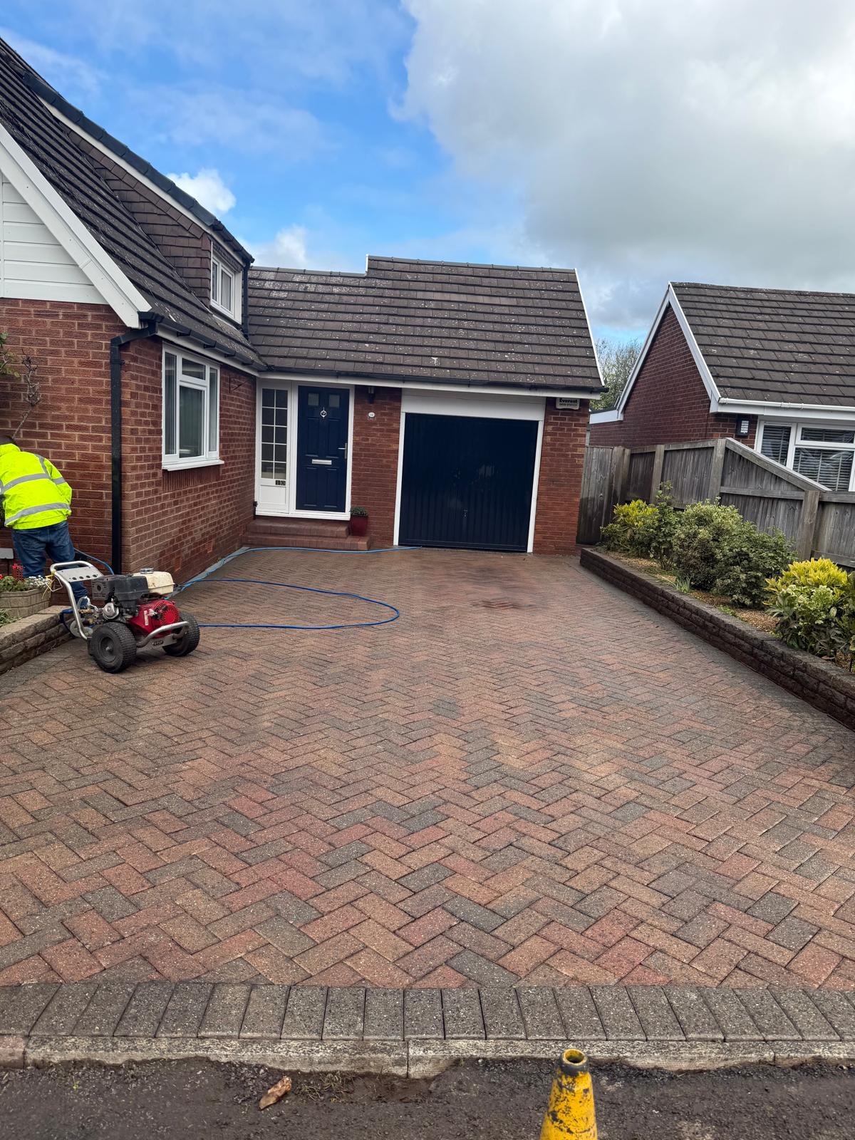 Operative in yellow hi-vis working on block-paved driveway