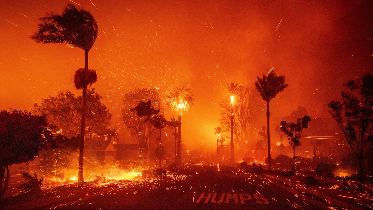 California wildfire approaching residential area with dramatic orange sky and flames in the hills