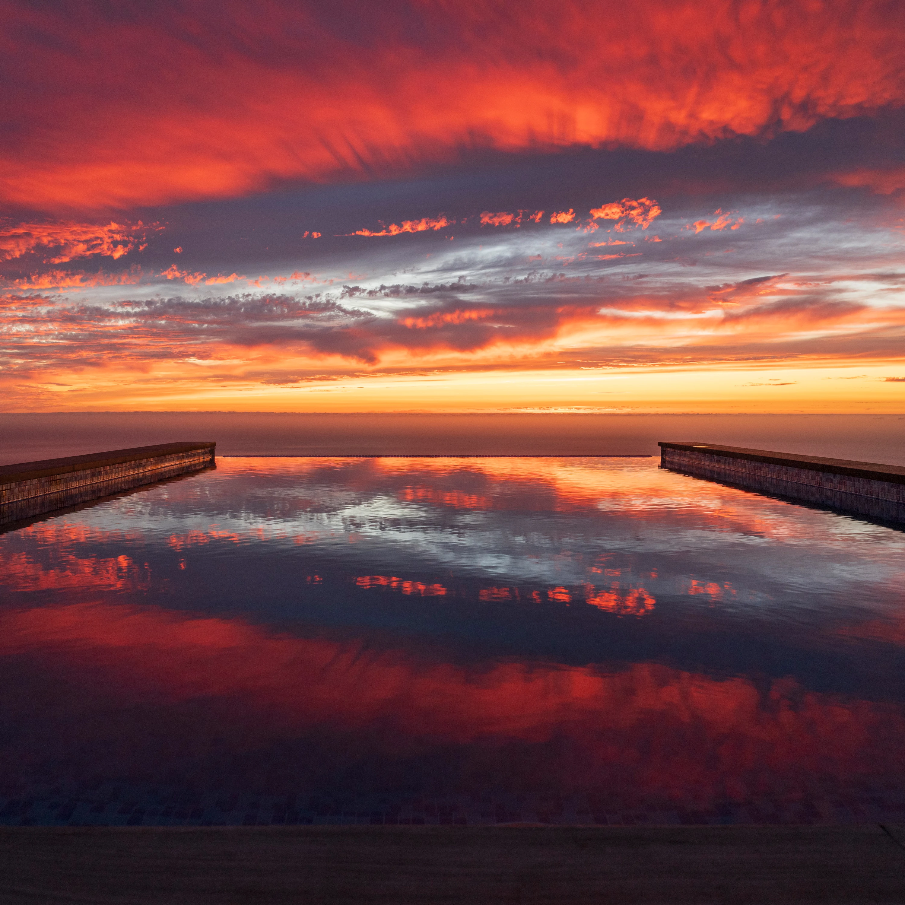 Infinity pool at sunset with dramatic red sky reflection