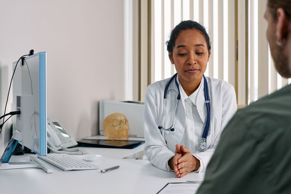 A Black female sleep medicine physician in a white coat with a stethoscope consulting with a male veteran patient in a clean clinical office
