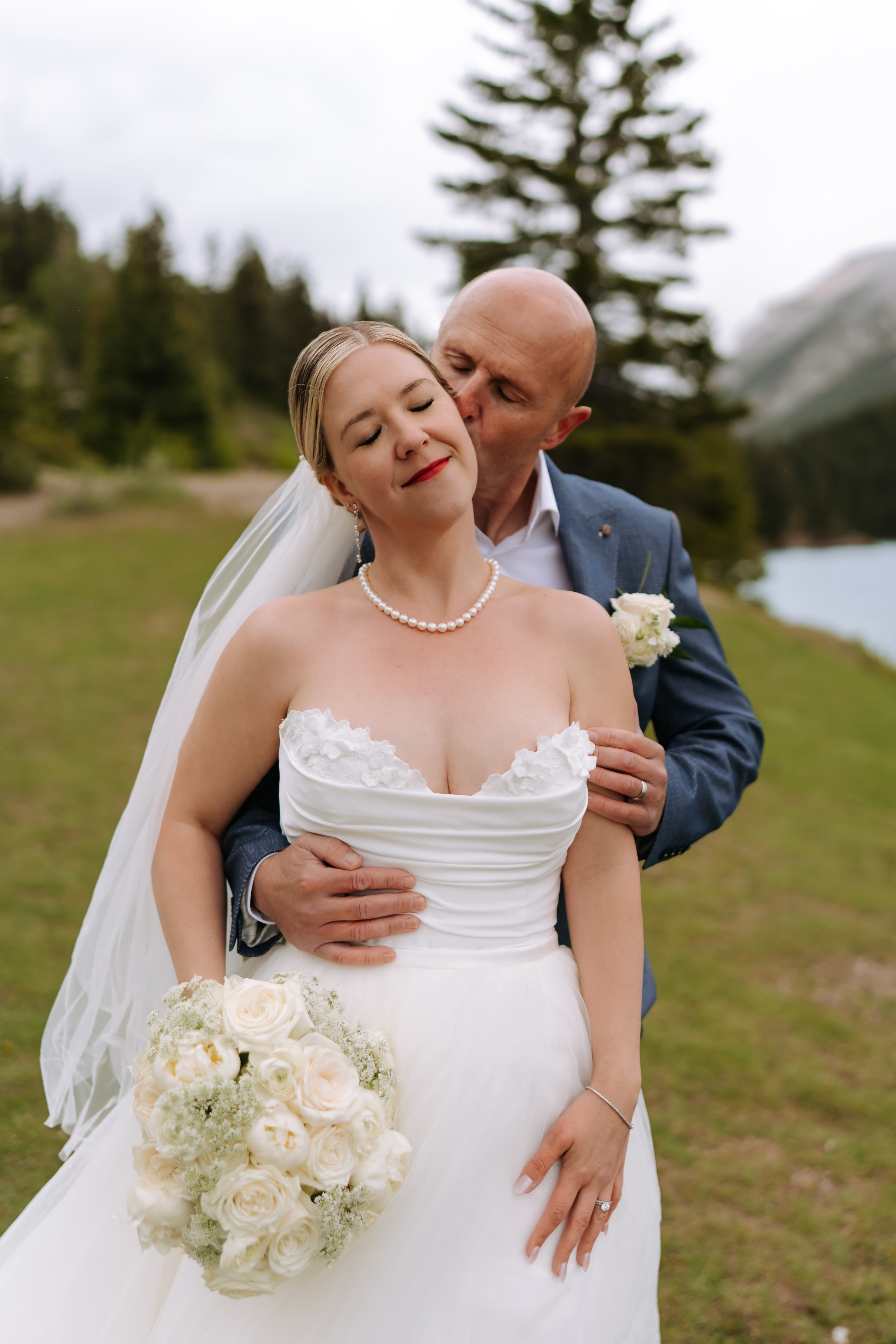 Bride and groom with classic white bouquet at mountain lakeside