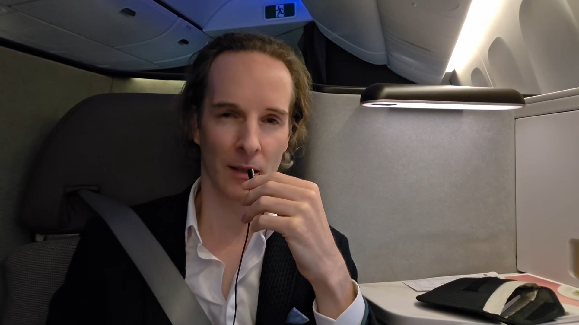 Felix Nikolas Prehn speaking from an aircraft seat in a dark jacket and white shirt, with a tablet on the side table