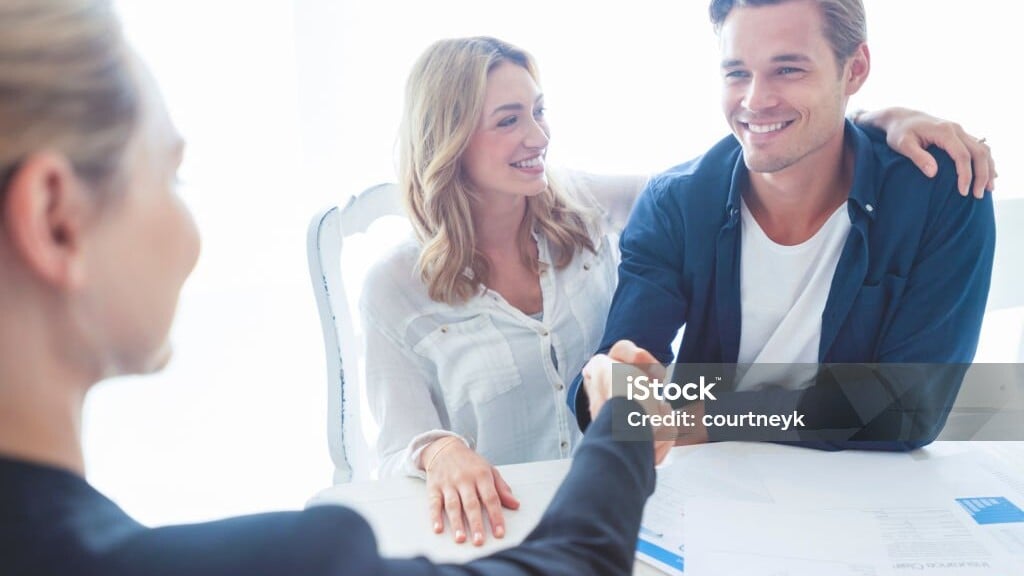 Real estate agent and happy clients at a closing table handshake