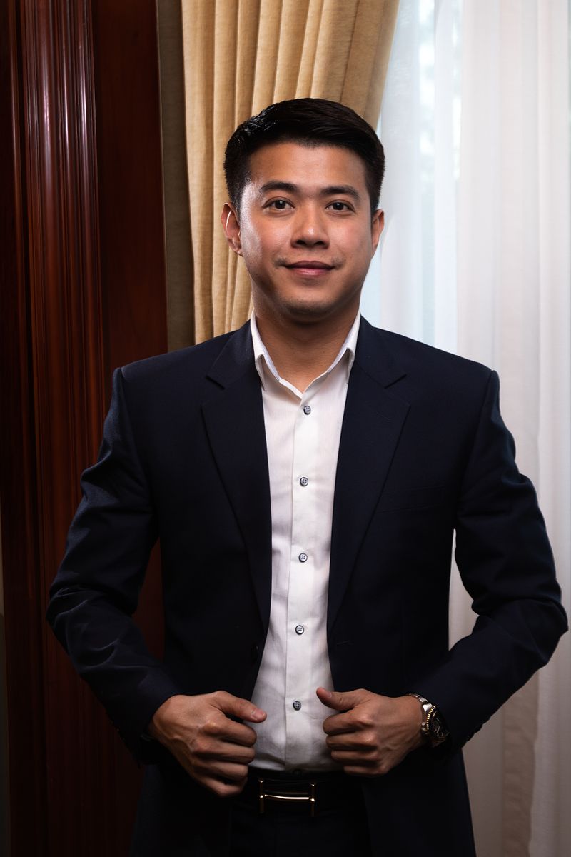 A confident Asian professional man in his 30s-40s in a dark blazer and white dress shirt, conveying a trustworthy advocate presence