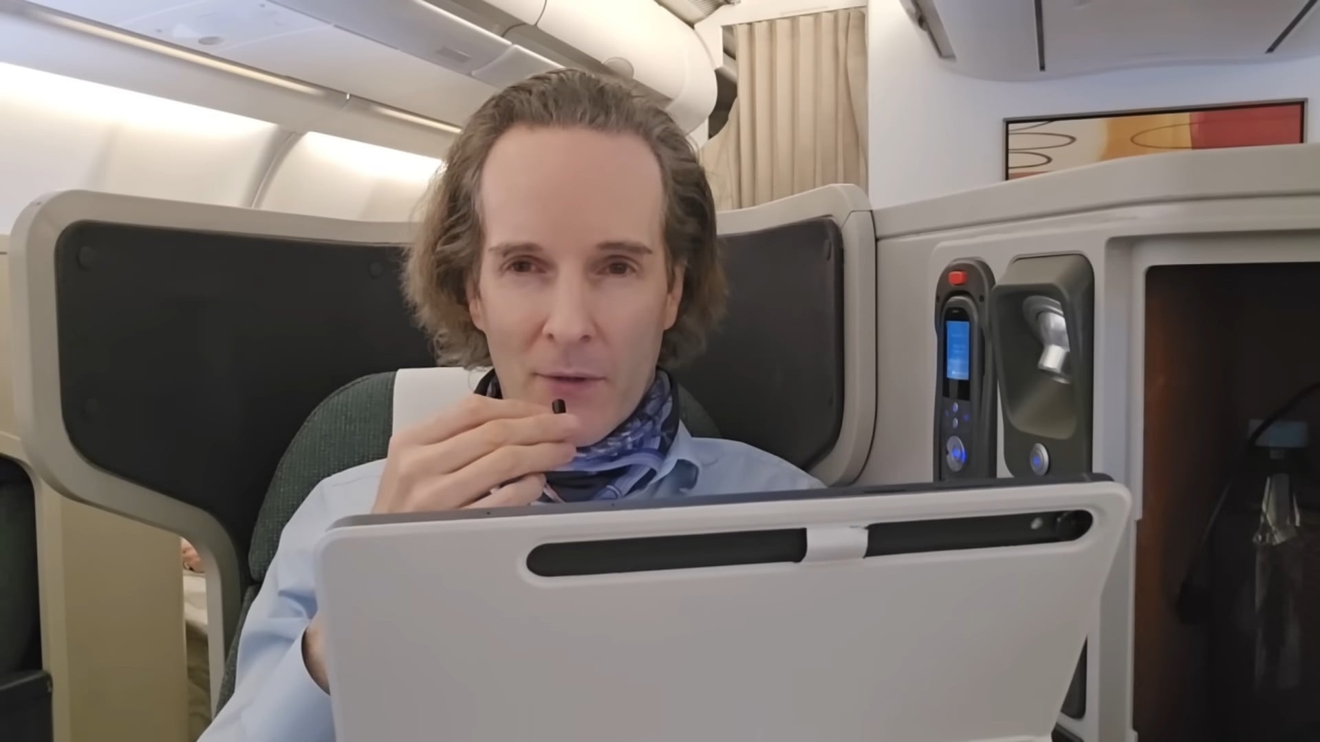 Felix Nikolas Prehn seated in an aircraft cabin with a tablet in front of him and a glass in one hand