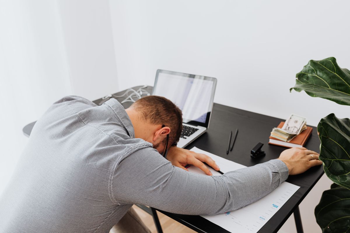 A man at an office desk with his head resting on his arms, unable to concentrate or stay awake due to the cognitive effects of chronic sleep deprivation