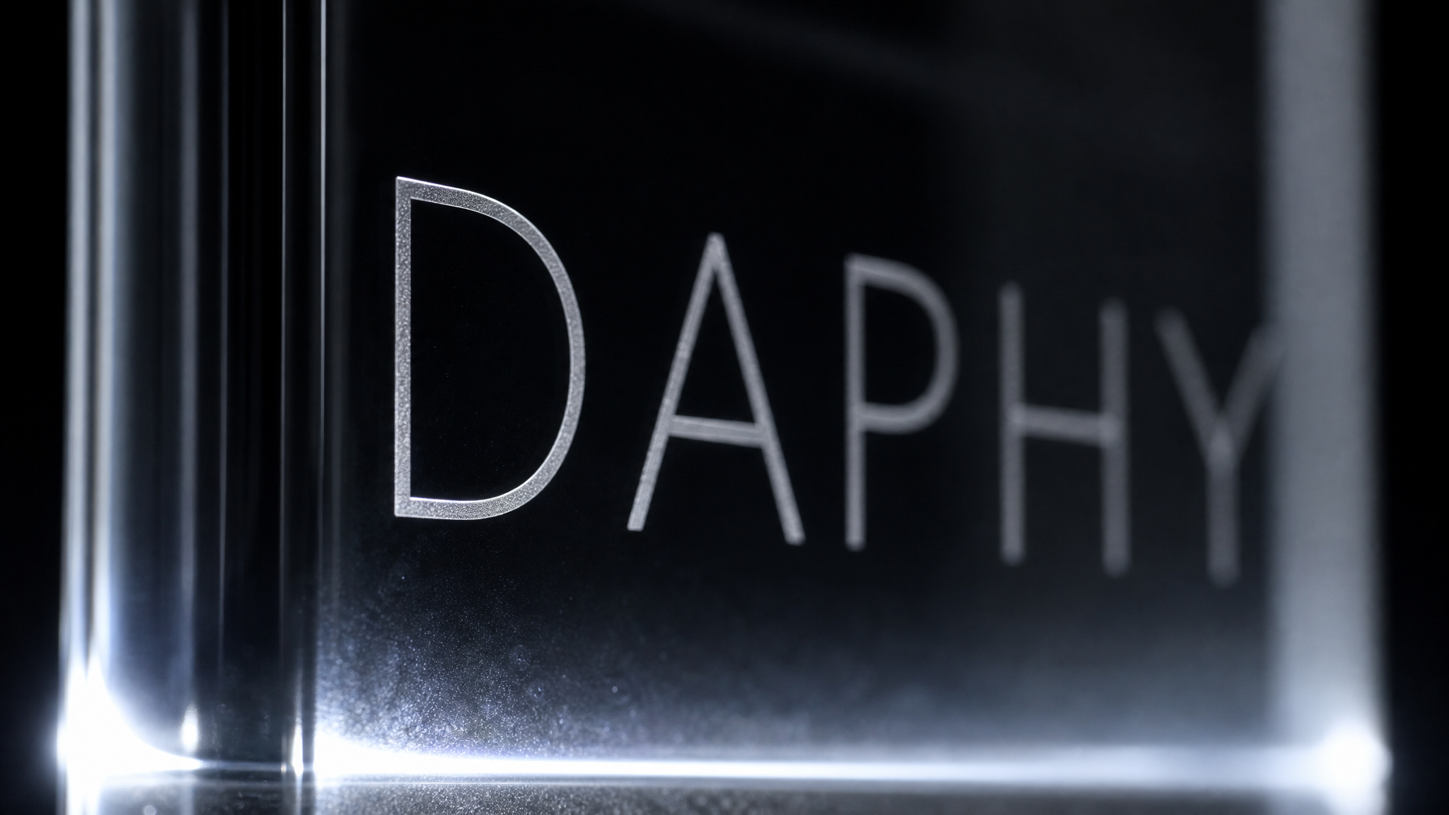 A name engraved into the thick front pane of the glass in fine, widely spaced uppercase letters, lit from below.
