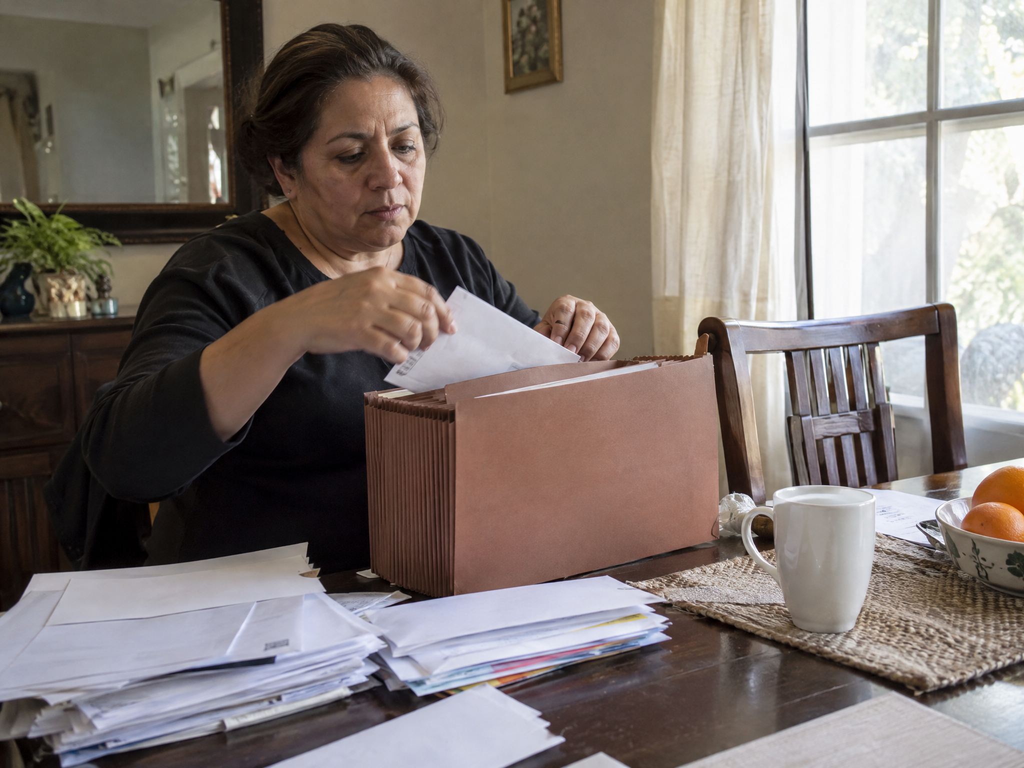 Veteran gathering records and envelopes into an accordion file at her dining table
