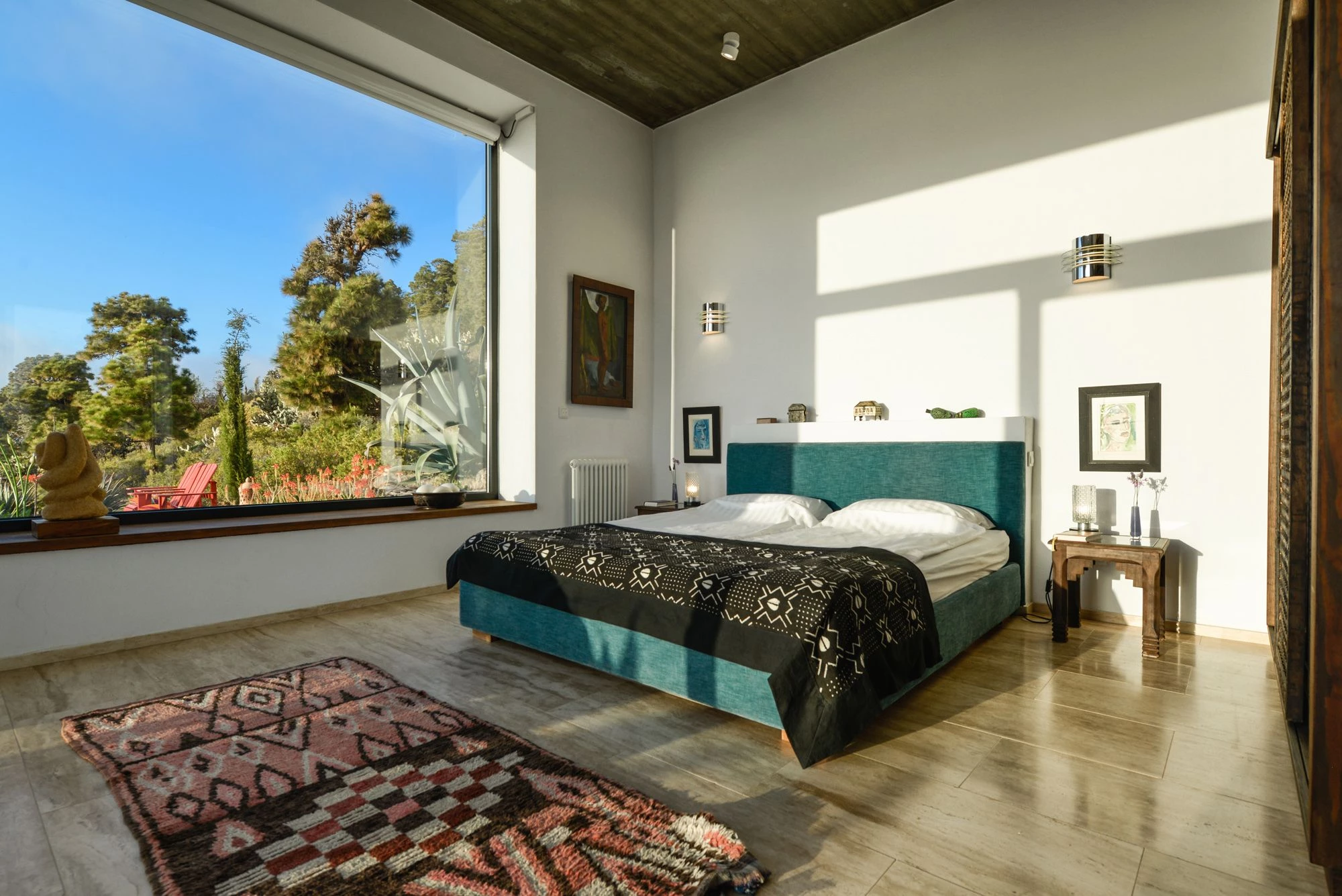 Bedroom with teal headboard, Moroccan rug, and large garden-view window