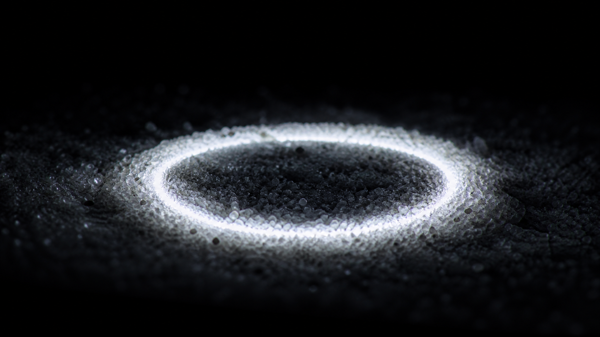 White light glowing upward through a layer of fine pale sea sand, each grain catching the light.