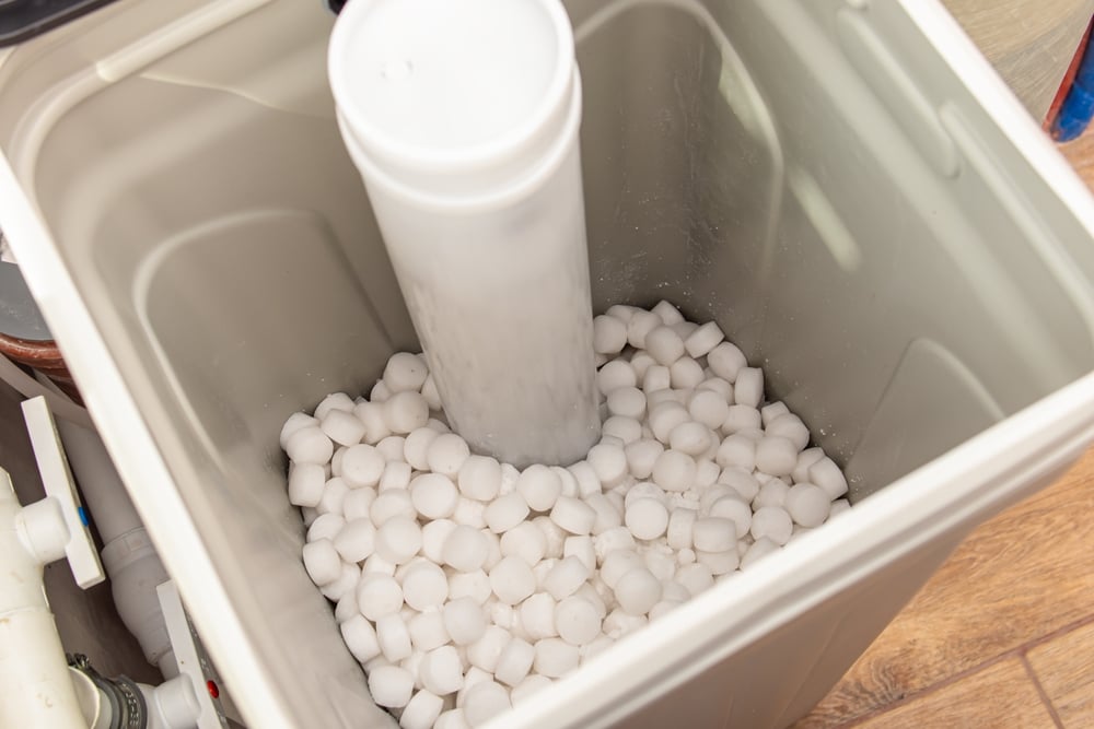 Homeowner adding salt pellets to water softener brine tank
