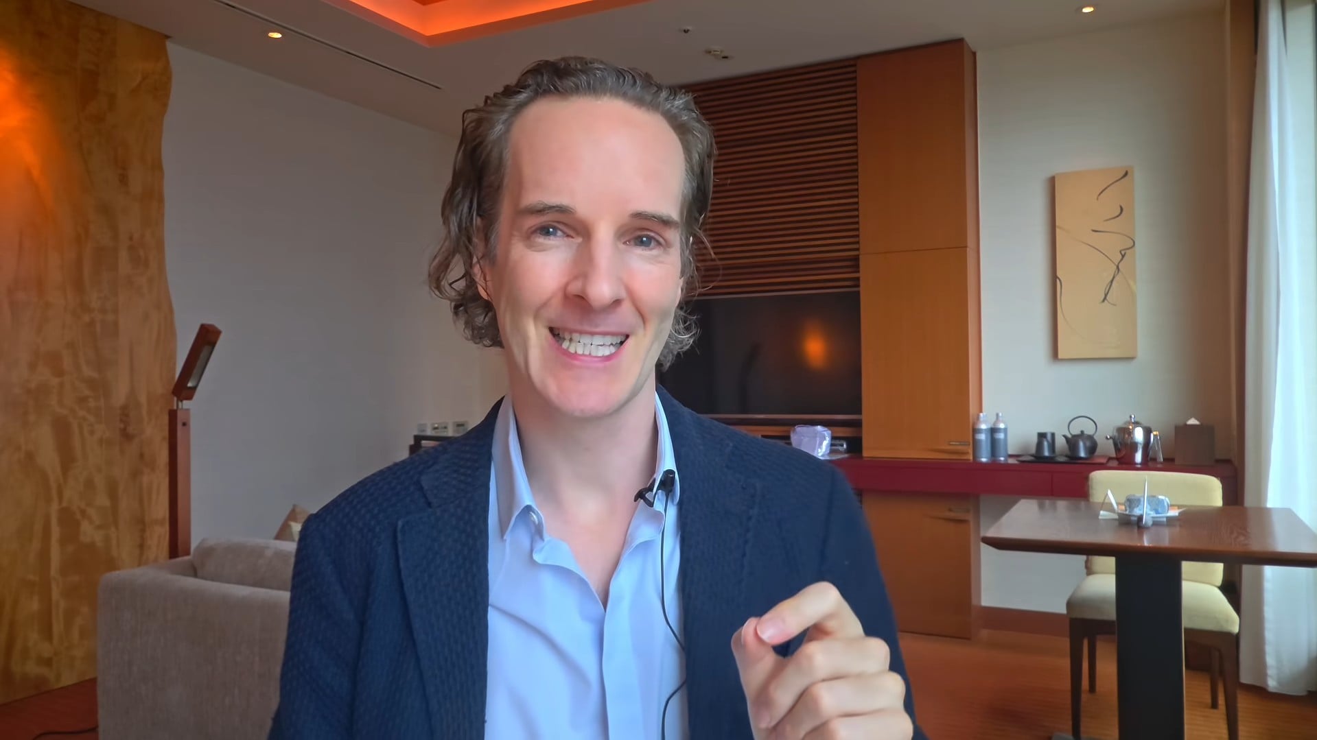 Felix Nikolas Prehn smiling in a navy jacket in a hotel sitting room with a dining table behind him