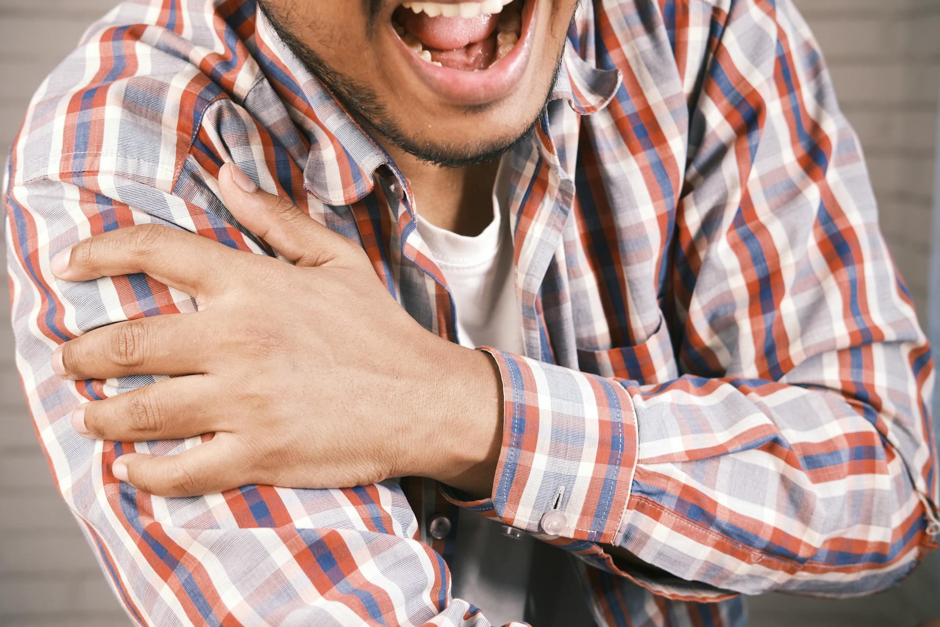A person grimacing and clutching their shoulder in pain, unable to carry a load due to shoulder weakness and giving way