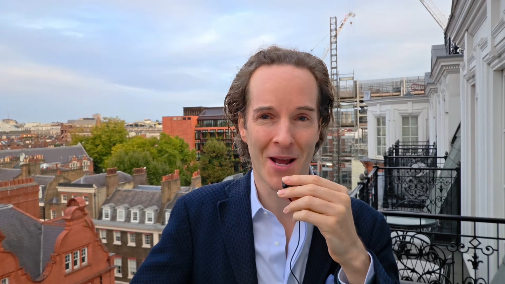 Felix Nikolas Prehn speaking from a London balcony, with red-brick buildings and rooftops in the background