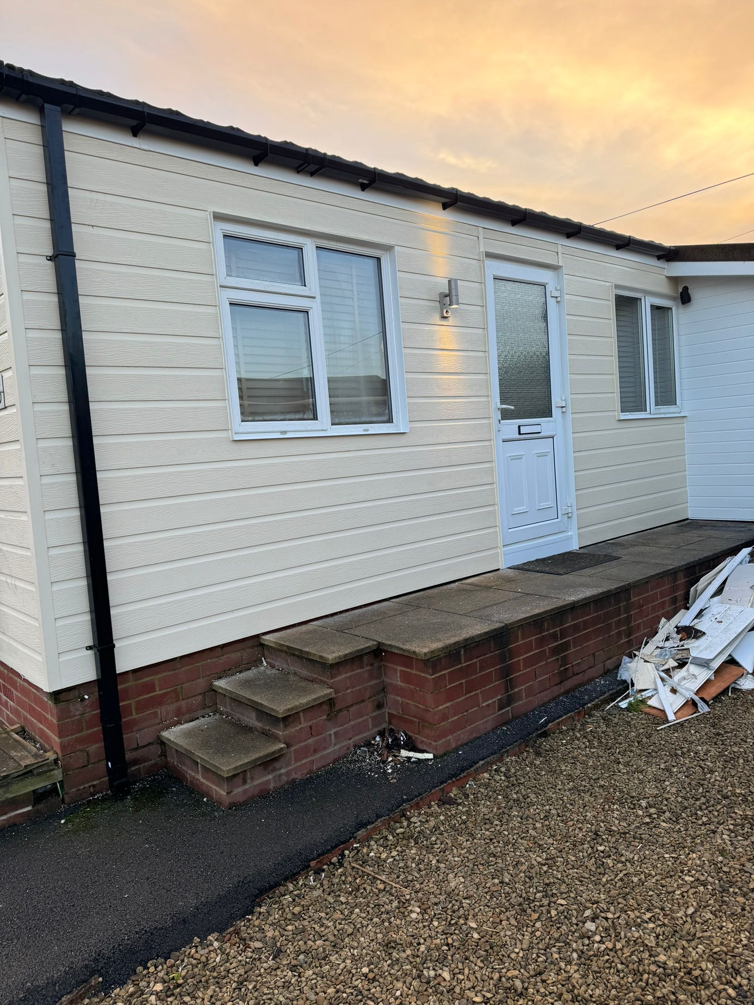 Completed park home with cream horizontal cladding, white door and new guttering at sunset
