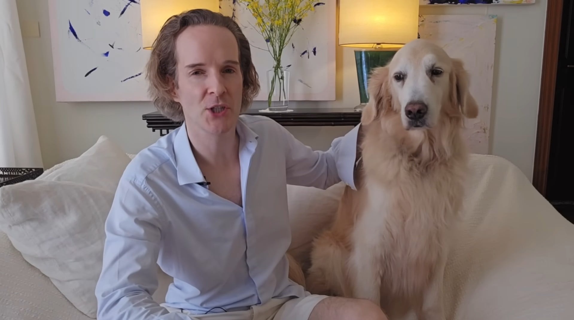Felix Nikolas Prehn seated on a sofa in a pale blue shirt, speaking beside his golden retriever Winston