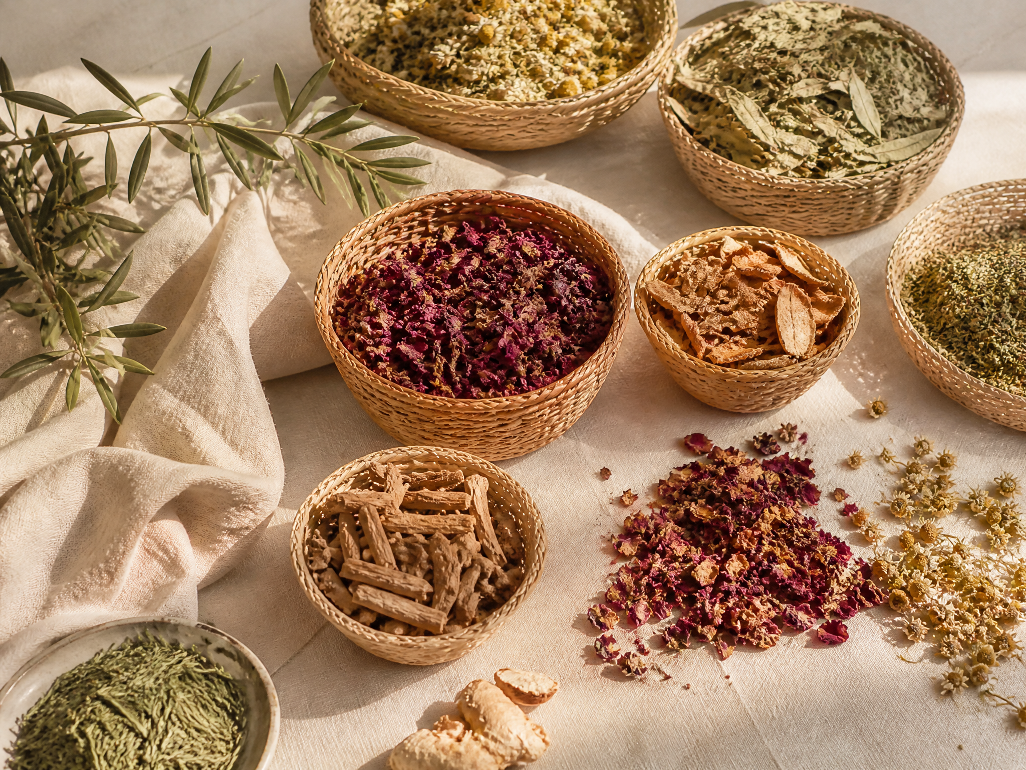 Baskets of dried botanicals, herbs, petals and citrus peel on warm ivory linen
