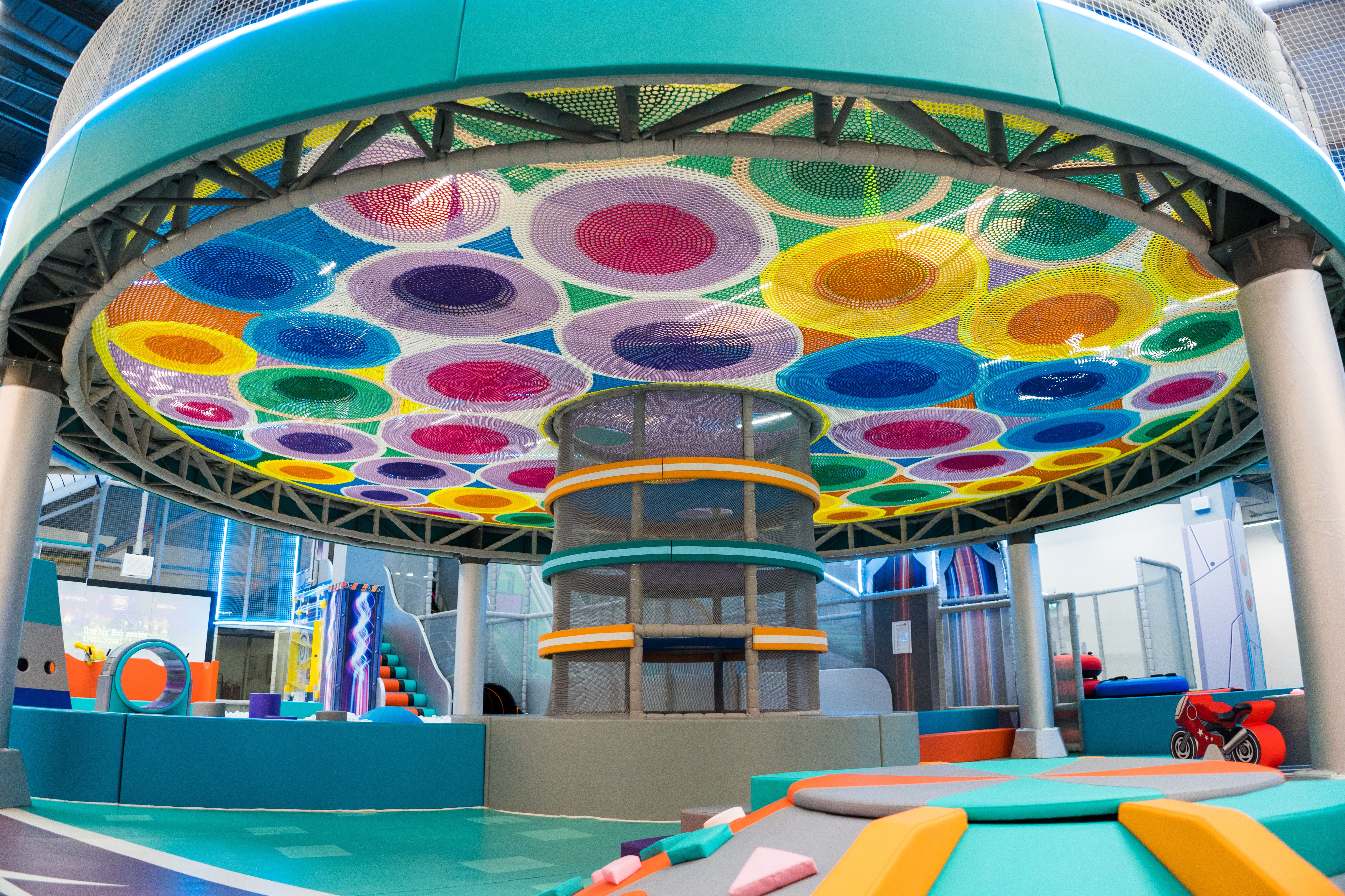 Colorful indoor play area with large climbing net canopy and circular patterns