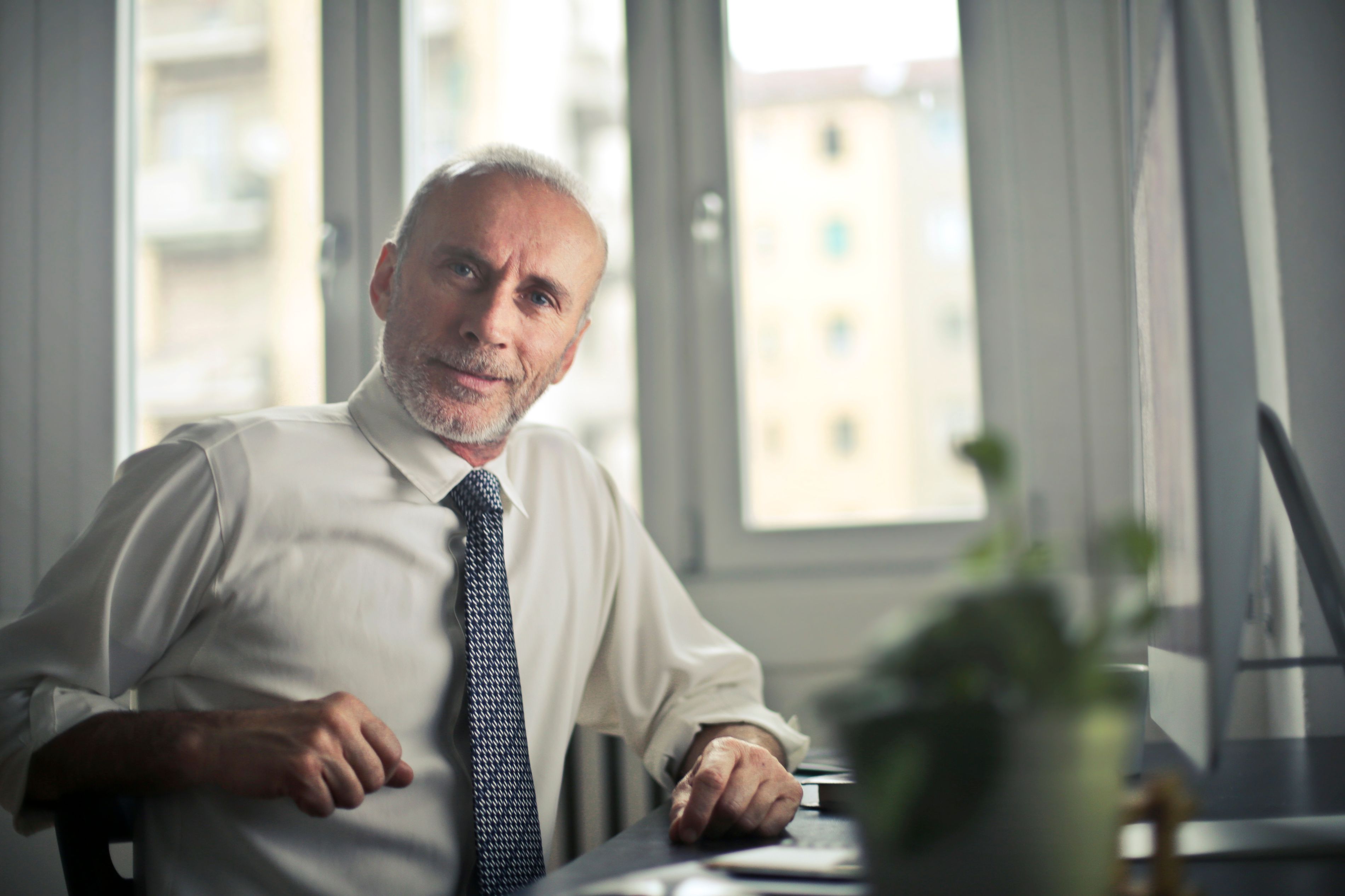 A confident professional man in his 50s in business attire seated in a bright office, conveying a calm, trustworthy advocate presence