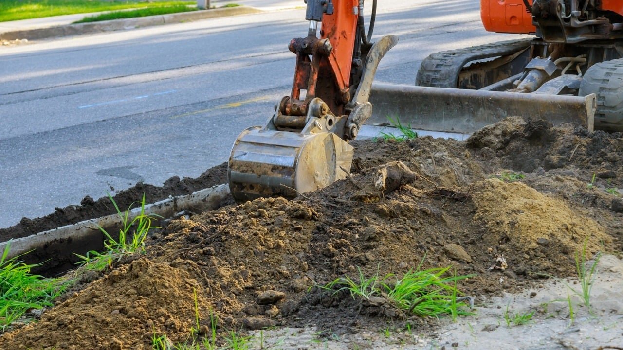 Tracked excavator digging utility trench along roadside