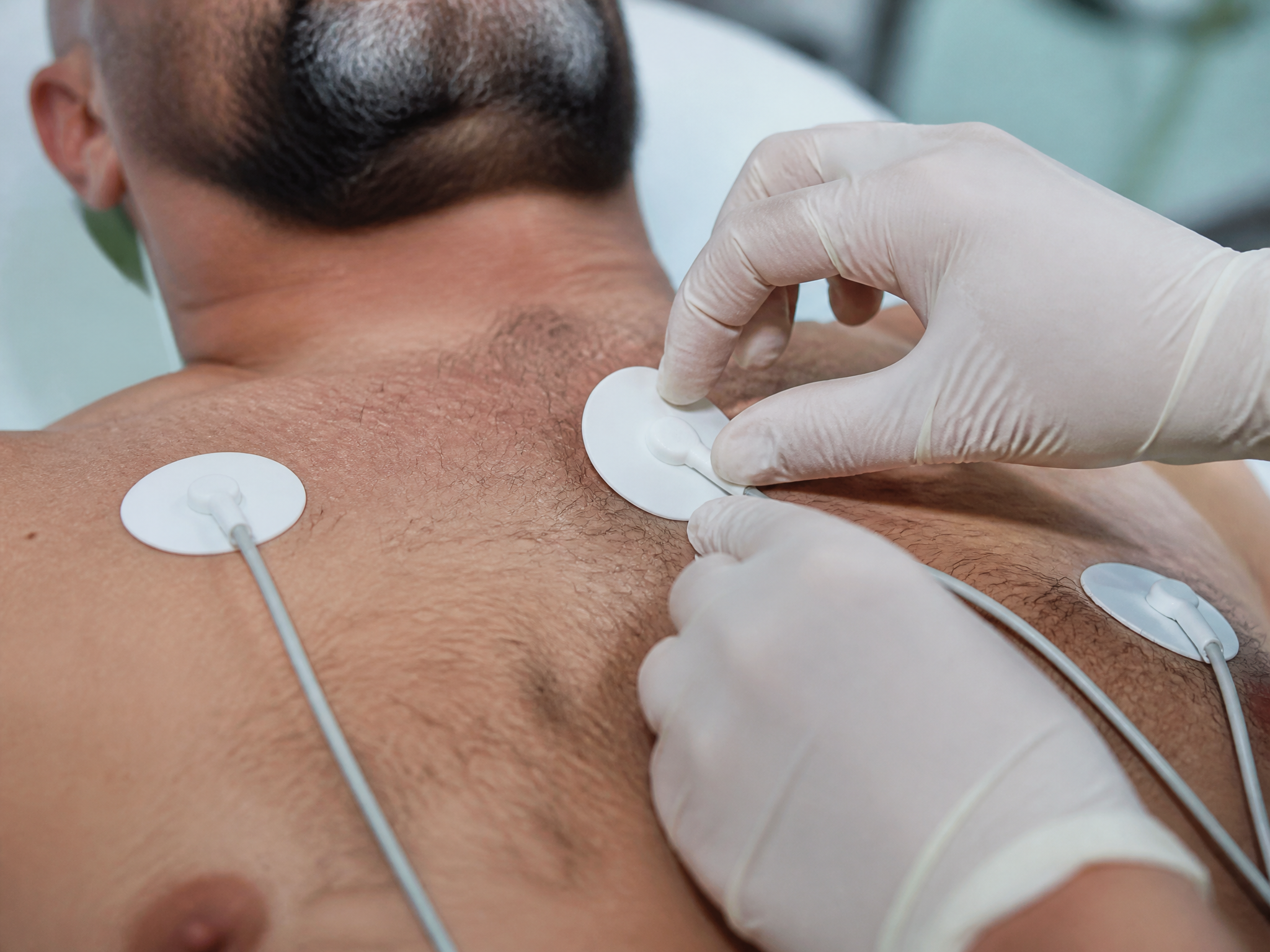 Close-up of ECG electrode pads being placed on a male veteran chest by gloved clinical hands in a medical setting