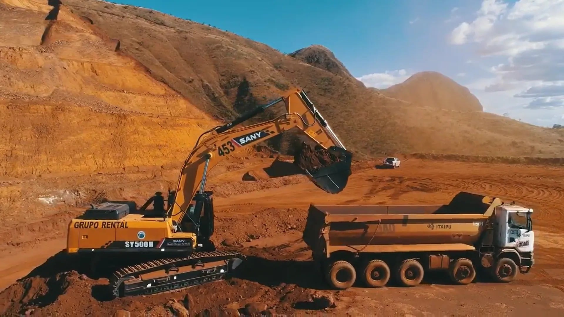 Excavator loading dump truck on large earthworks site at golden hour