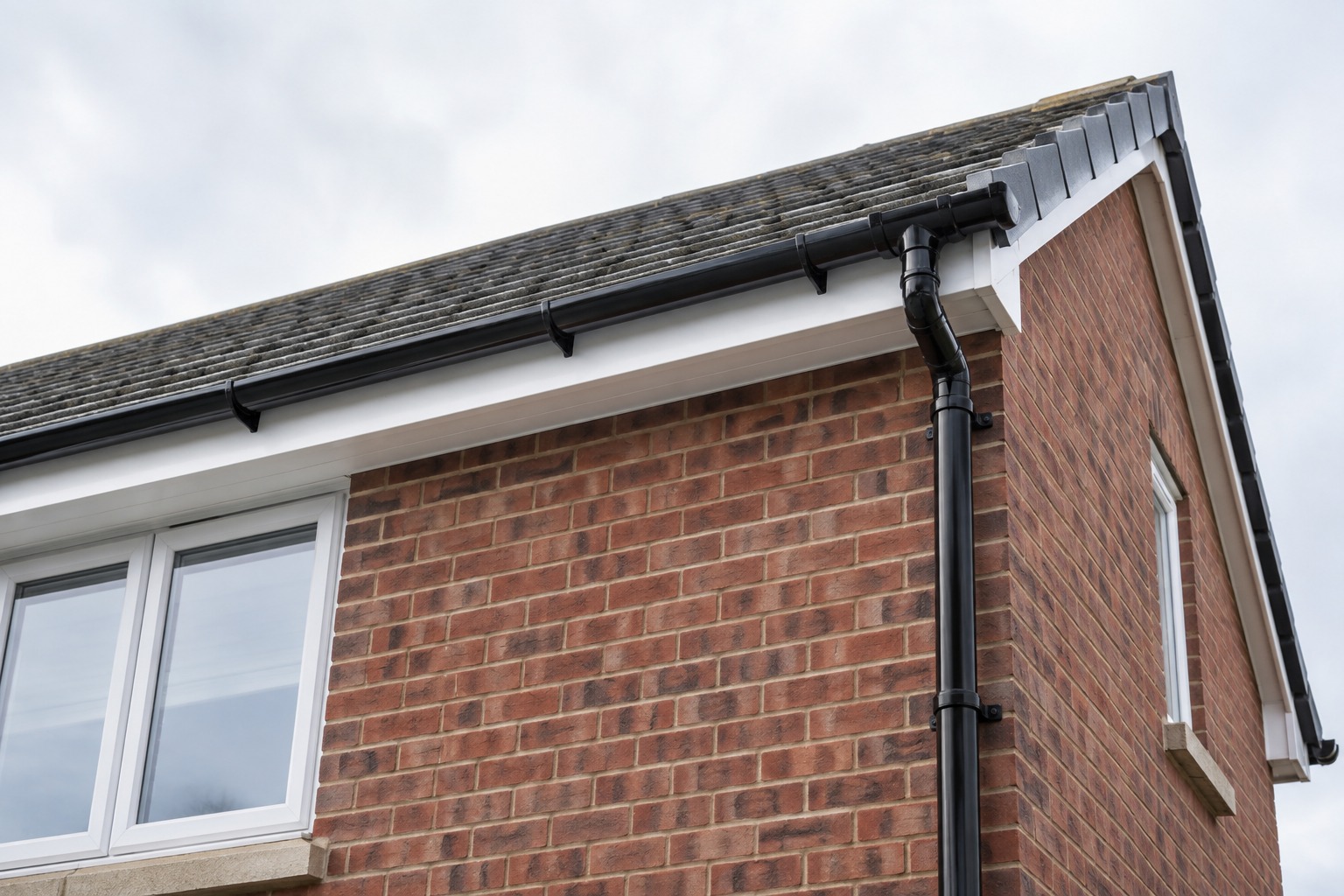 Black guttering and downpipe on a brick house gable