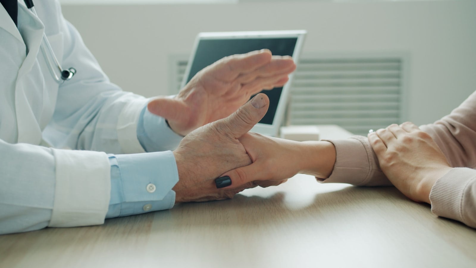 A physician holding an older patient's hand across a desk during an empathetic medical consultation