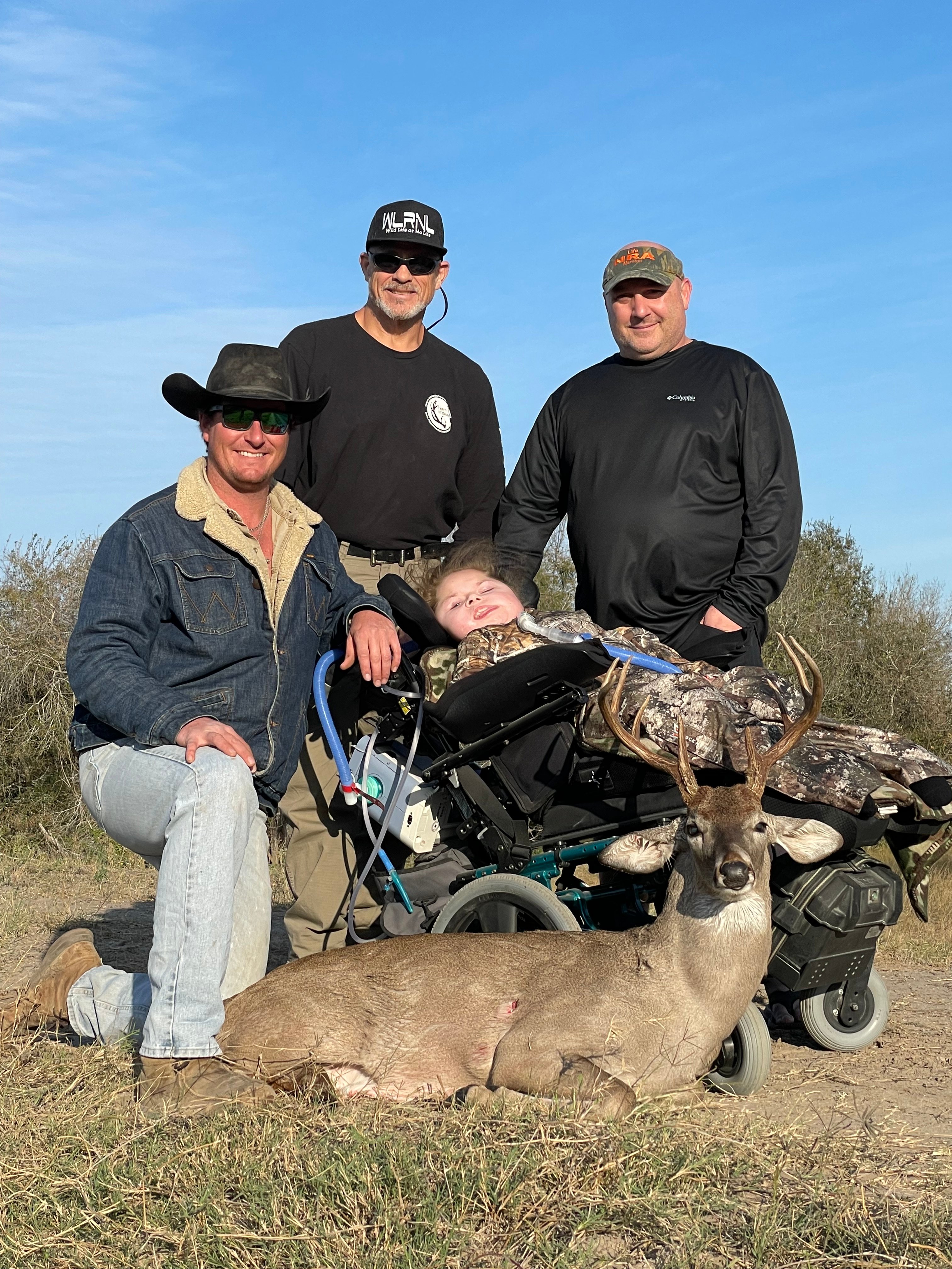 Three men with whitetail buck including wheelchair hunter in open field