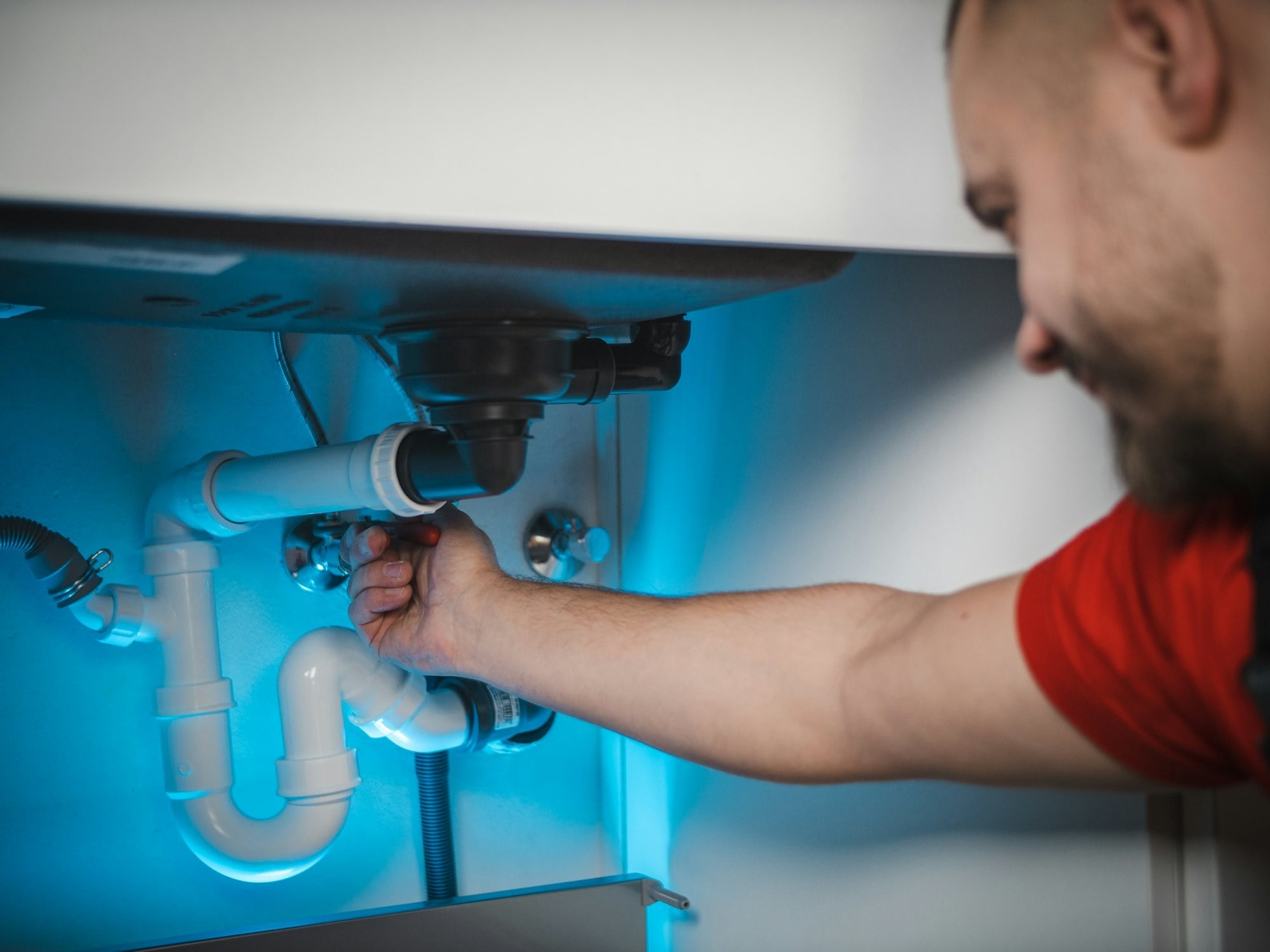 Emergency plumber repairing a leak under a kitchen sink