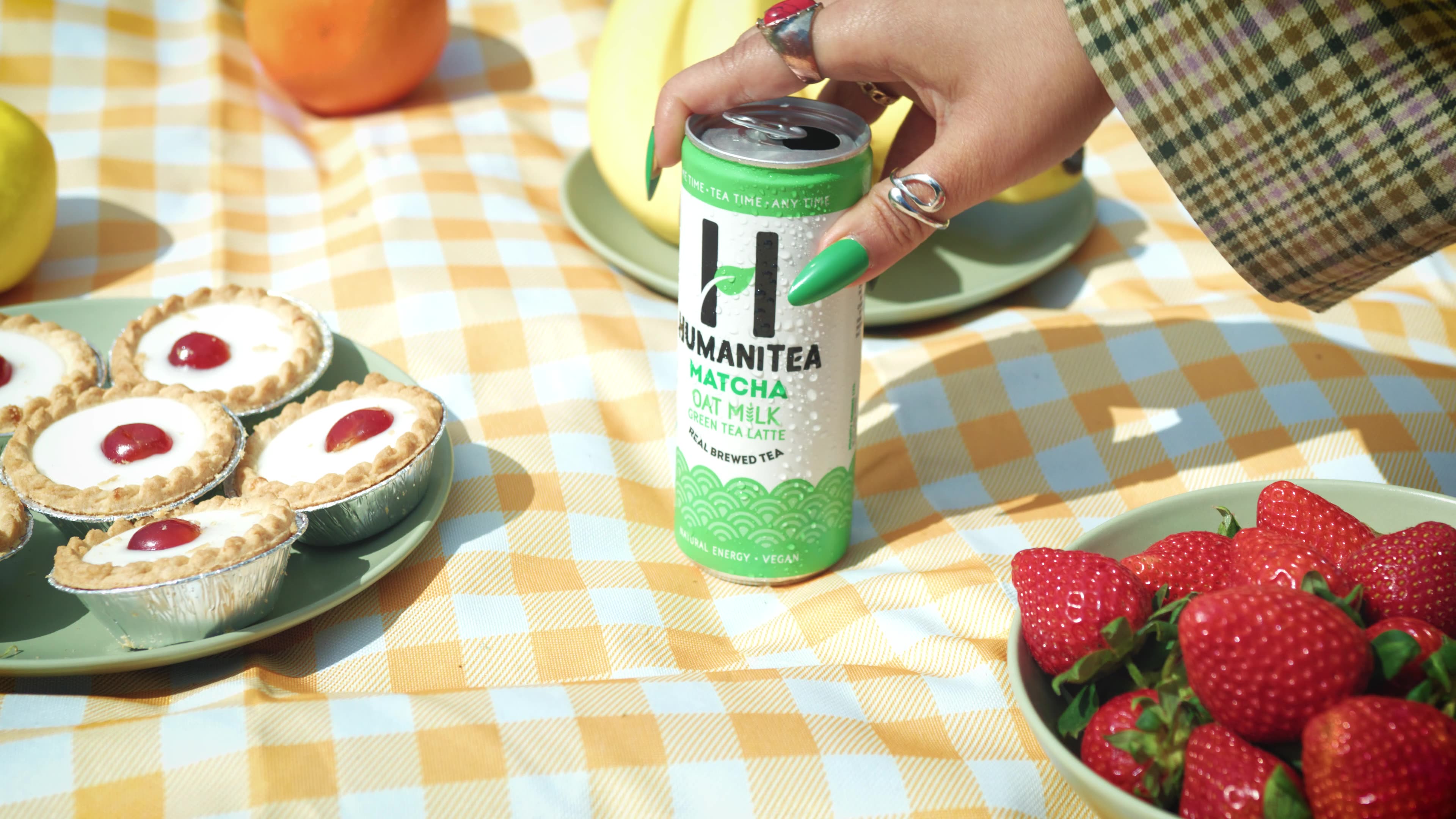 HumaniTea can on a picnic blanket with strawberries and tarts