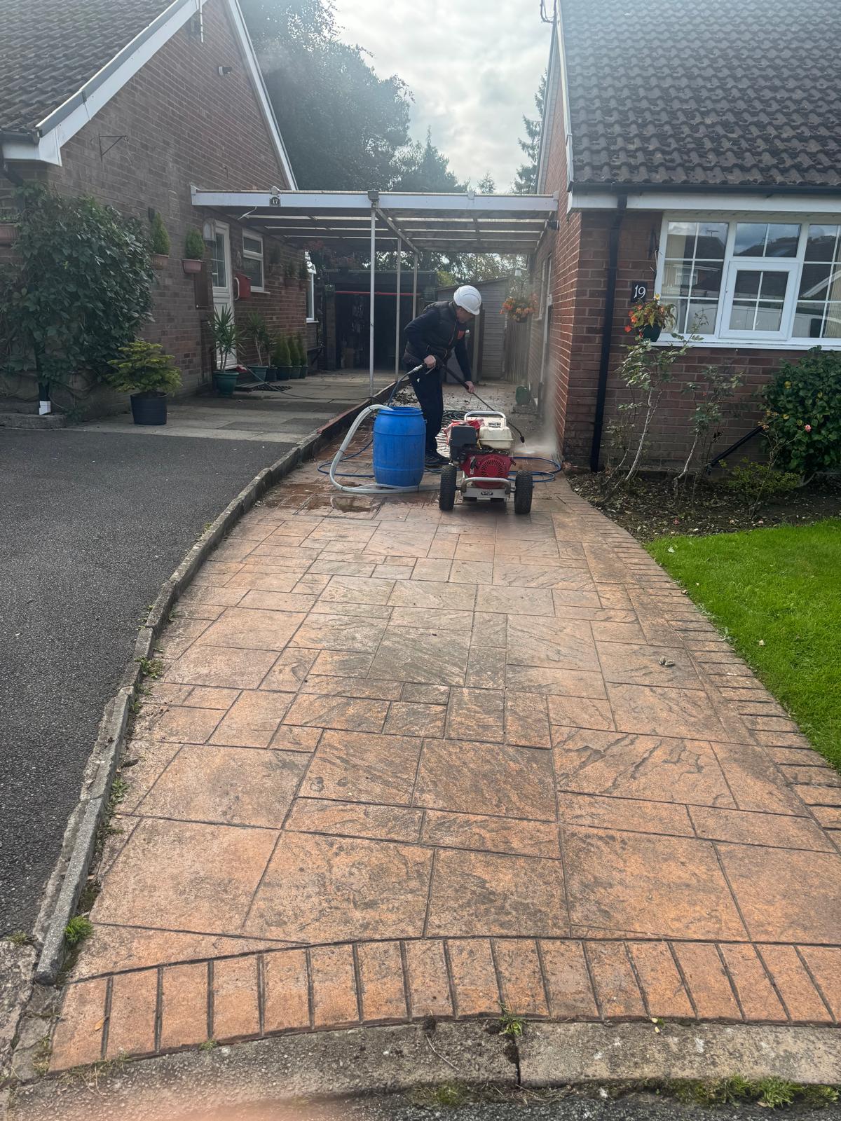 Worker pressure washing stamped concrete driveway at UK bungalow