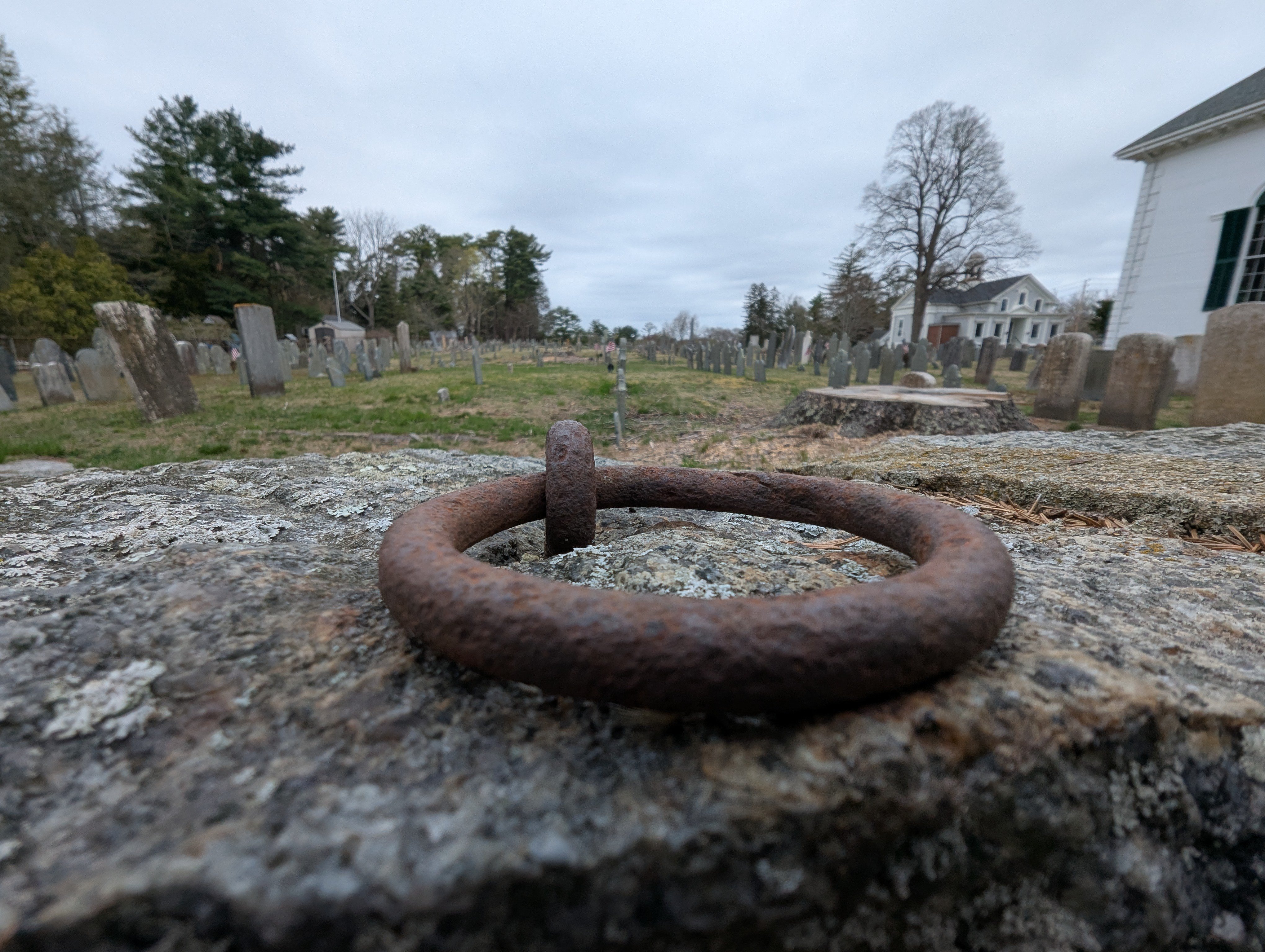 Iron hitching ring embedded in granite wall at Kingston Old Burying Ground with historic gravestones and church in background