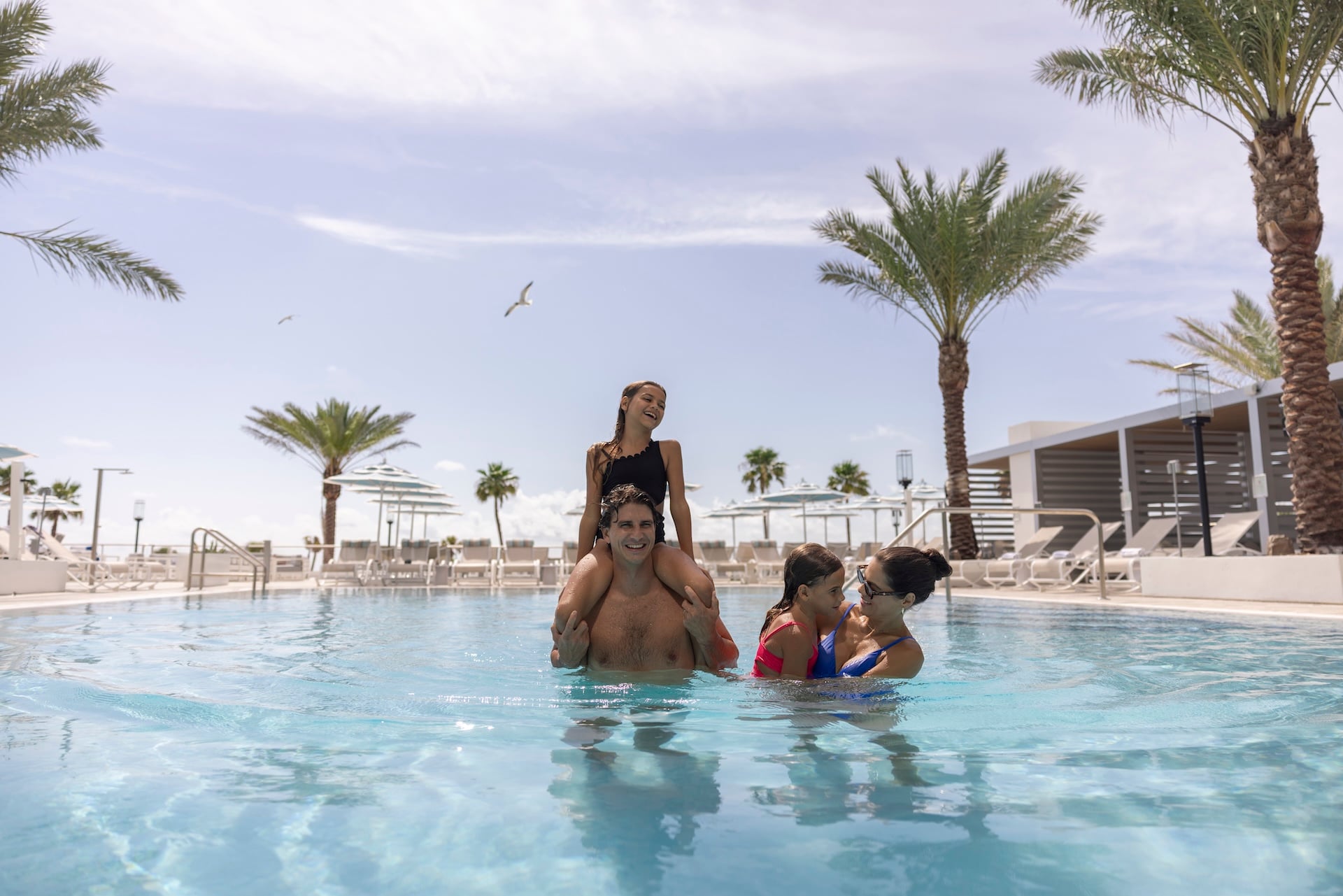 A family enjoying a palm-lined resort pool on a sunny afternoon