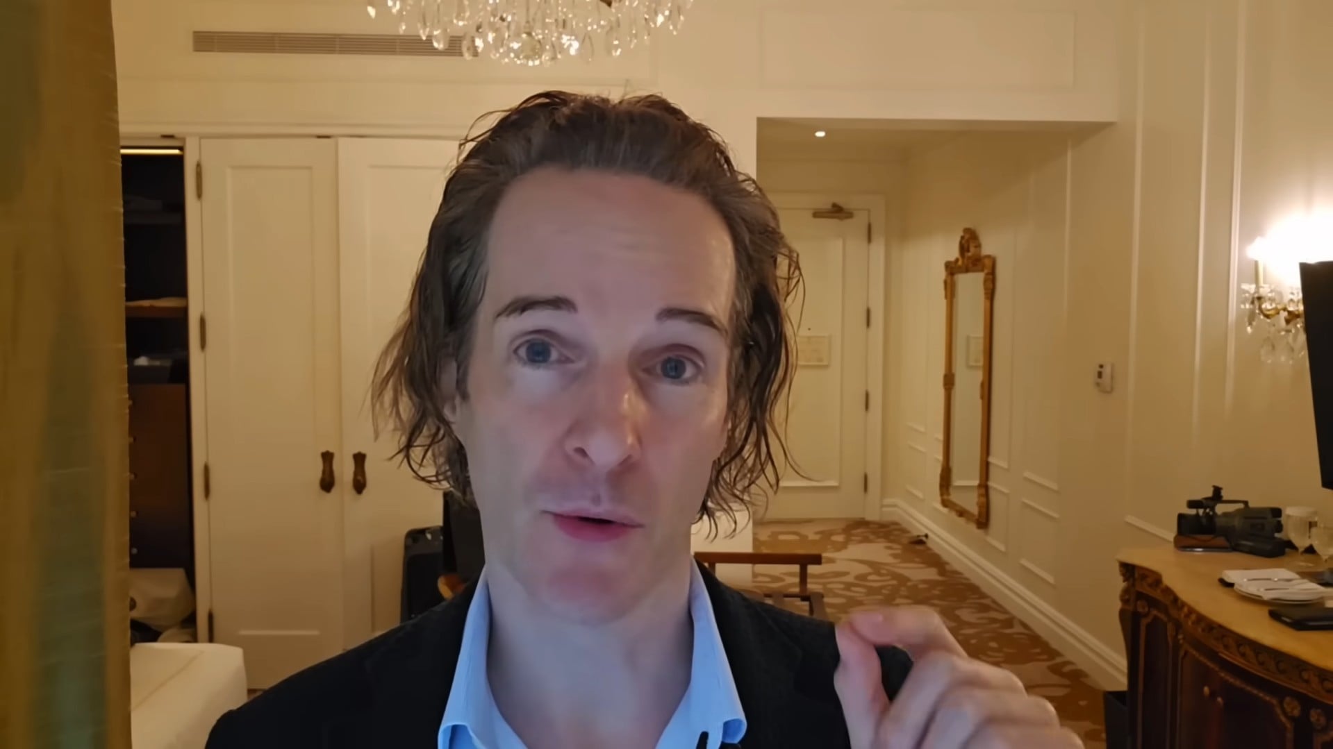Felix Nikolas Prehn speaking in a dark jacket in a warmly lit hotel corridor with panelled doors