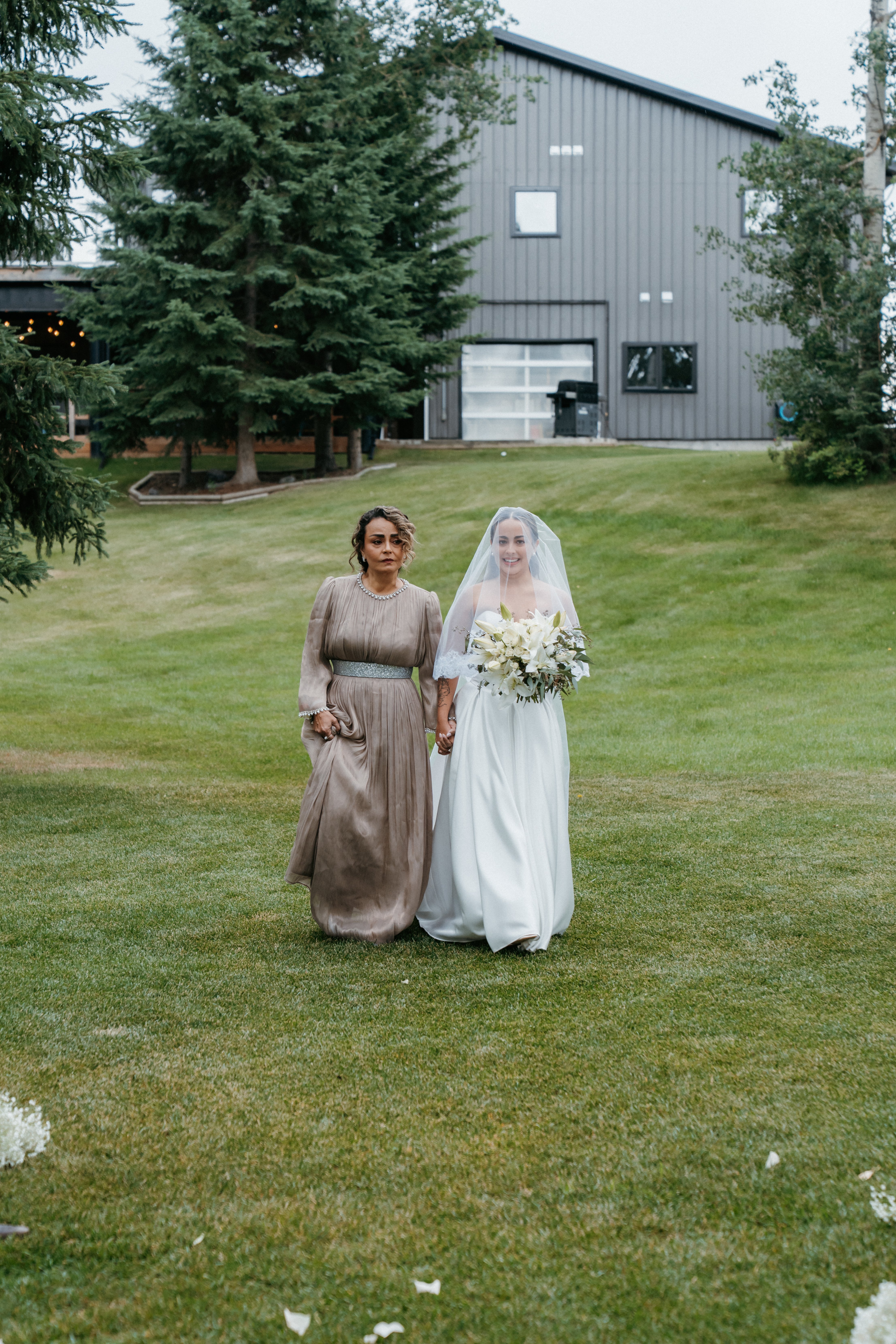 Bride walking with mother holding bouquet at outdoor venue