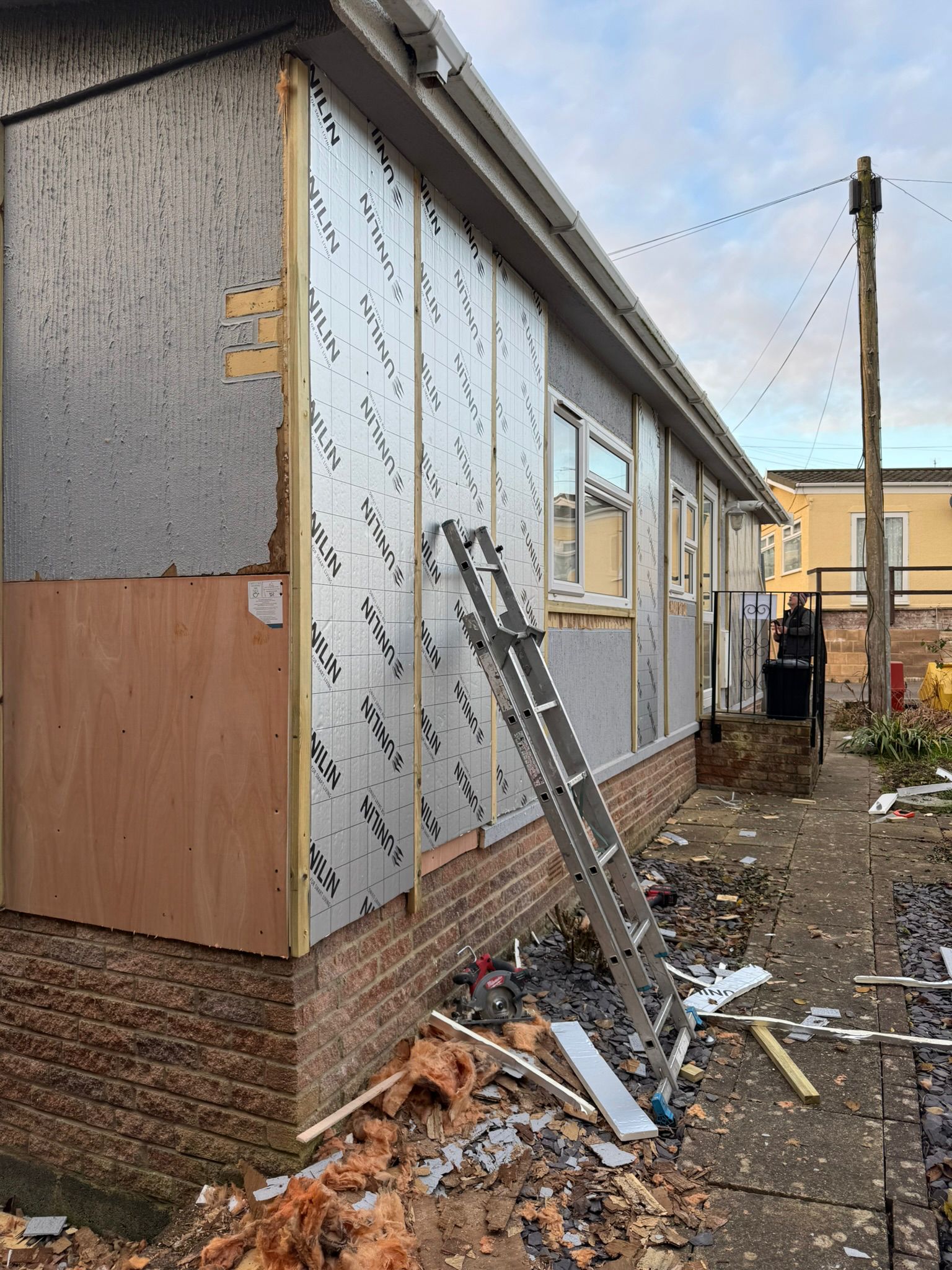 Insulation boards being fitted along park home exterior with ladder and old cladding removed