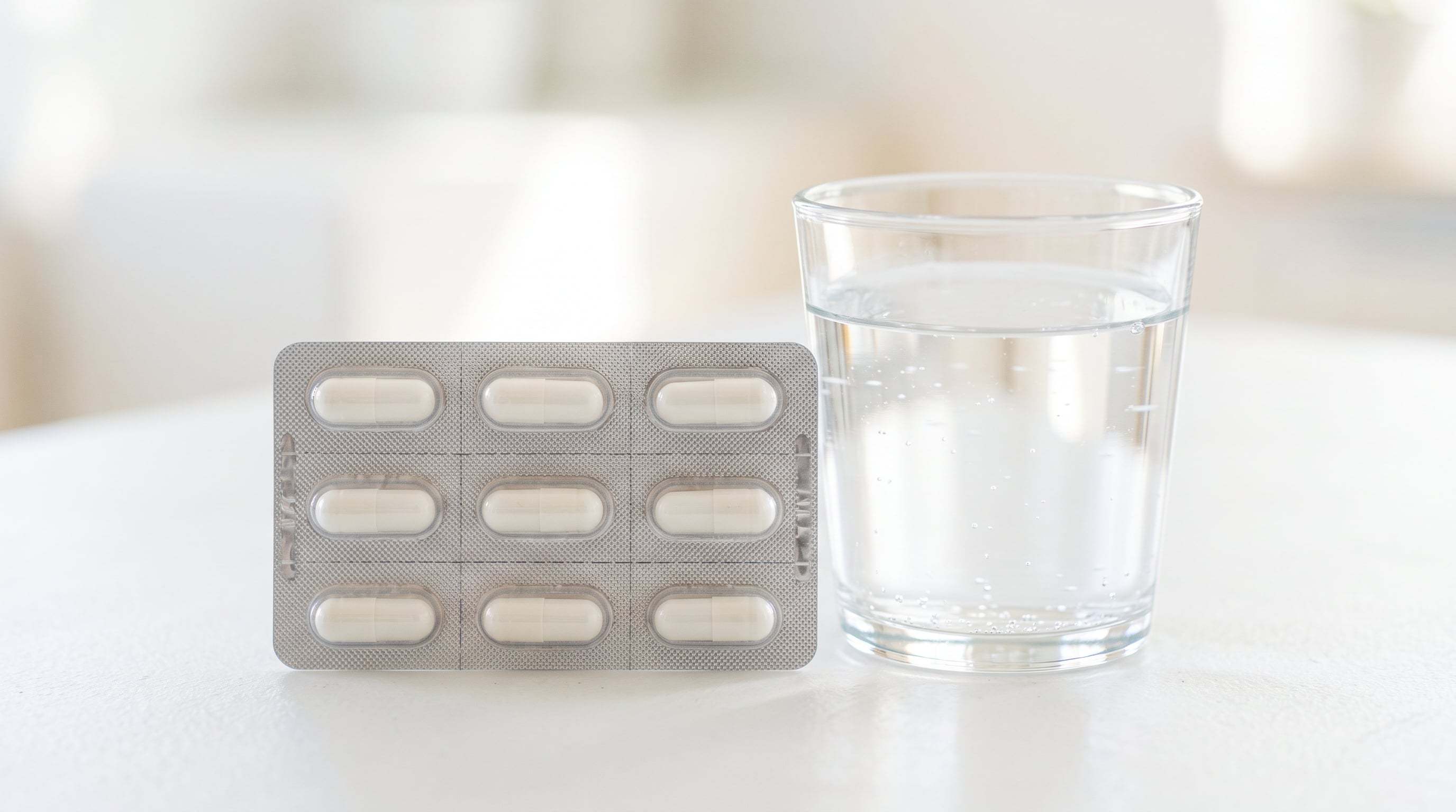 Antibiotic capsules in a sealed blister pack beside a glass of water on a white surface