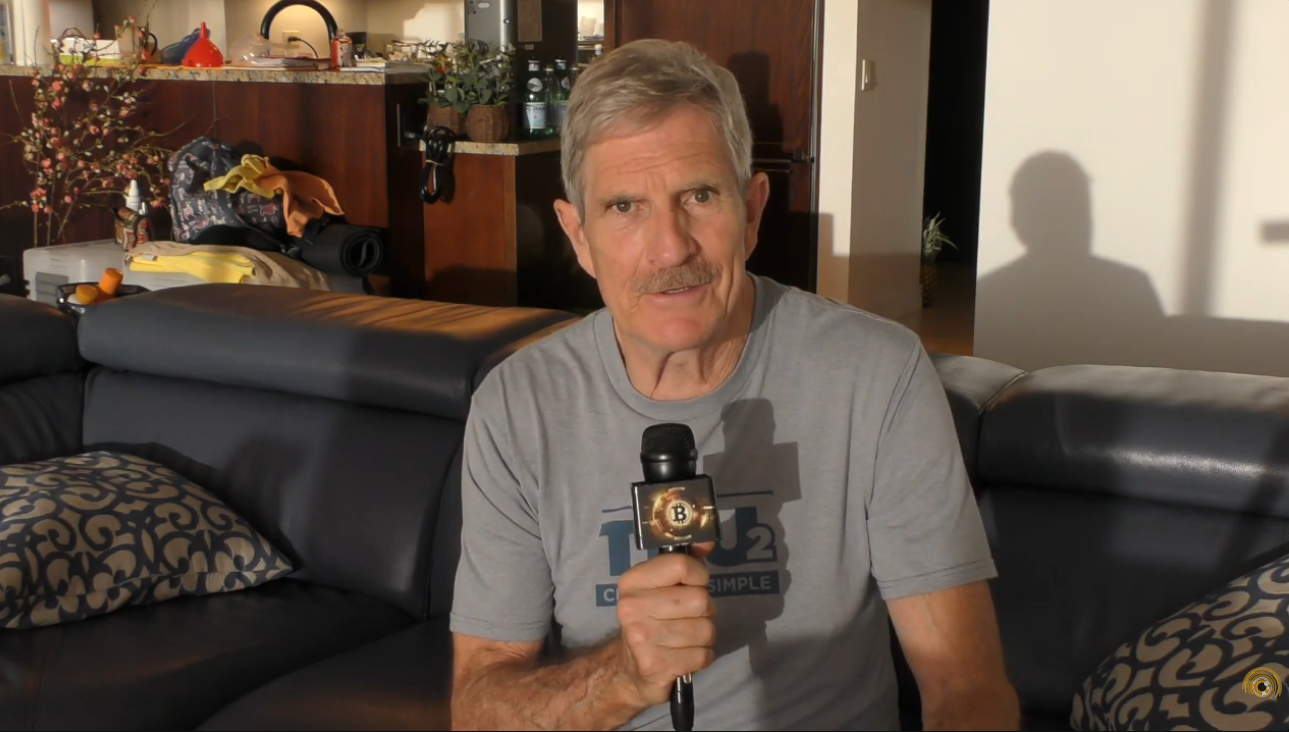 Dick at his Hawaii home holding a Bitcoin microphone flag on the lanai