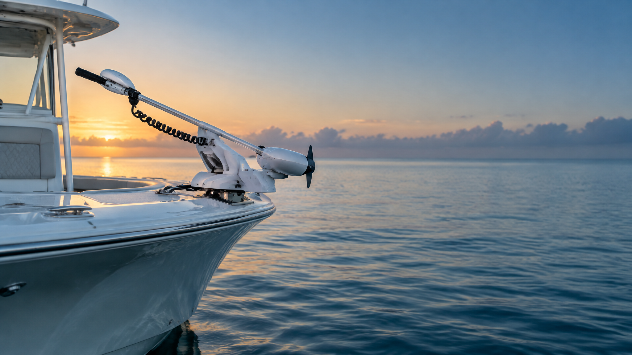 White bow-mounted saltwater trolling motor installed on the bow of a center-console fishing boat at dawn.
