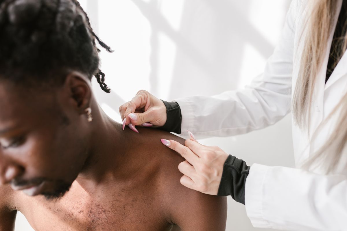A clinician examining a veteran patient's upper back and neck area during a physical assessment in a clinical setting