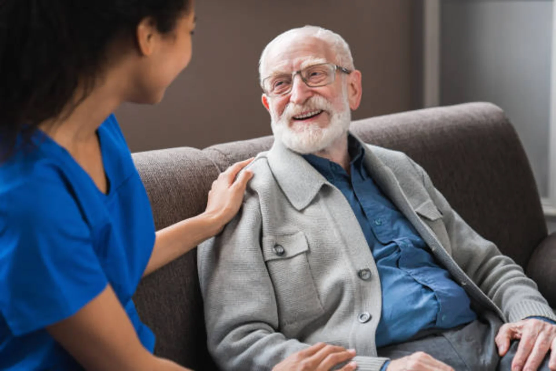 Professional African American female caregiver warmly engaging with happy elderly senior male patient in comfortable home setting, demonstrating compassionate in-home health care services in Los Angeles