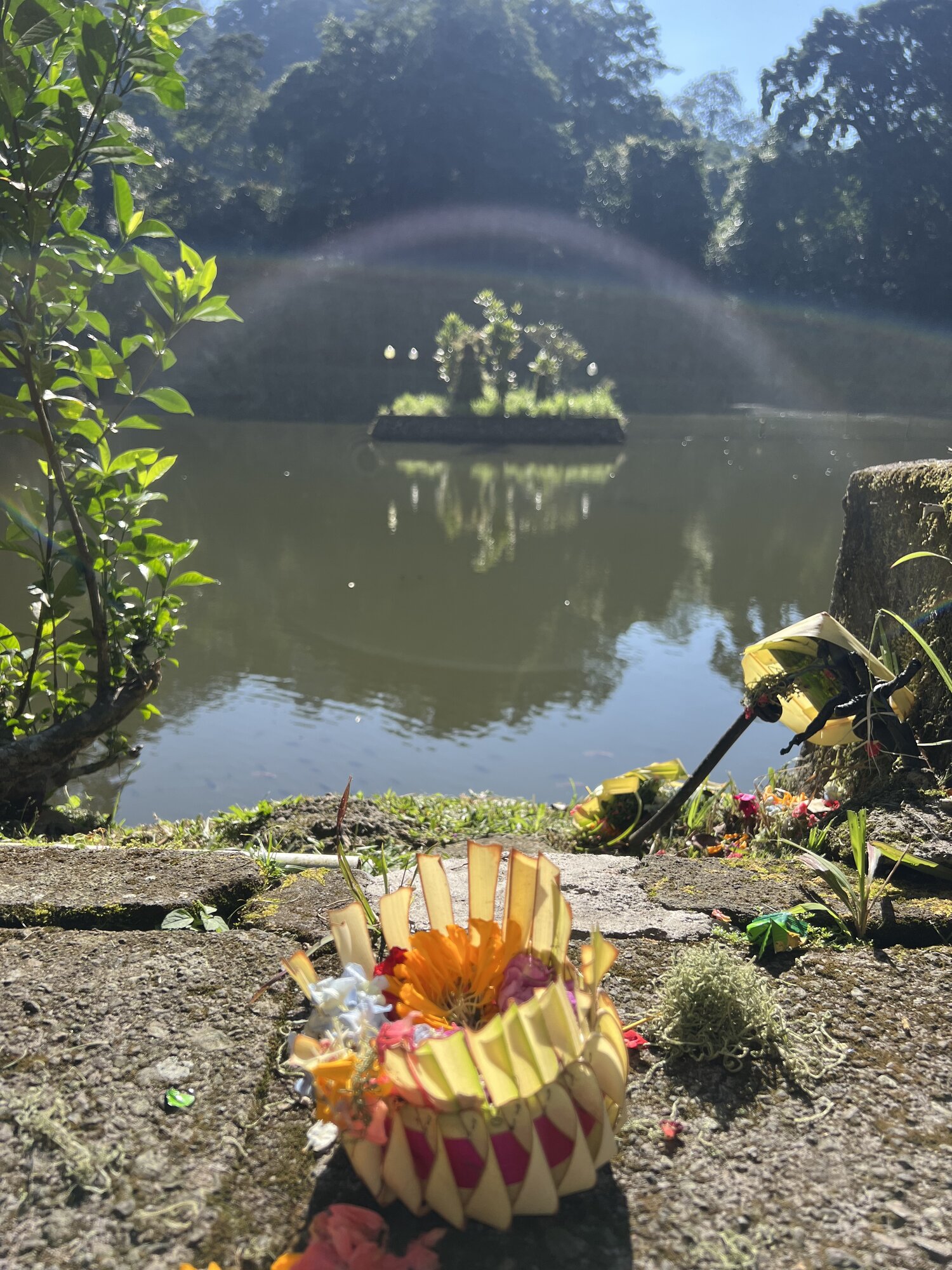 Sacred pond at Pura Luhur Batu Karu temple with traditional Balinese canang sari offering and fountain — start of the UNIKAT Green Escape e-bike tour