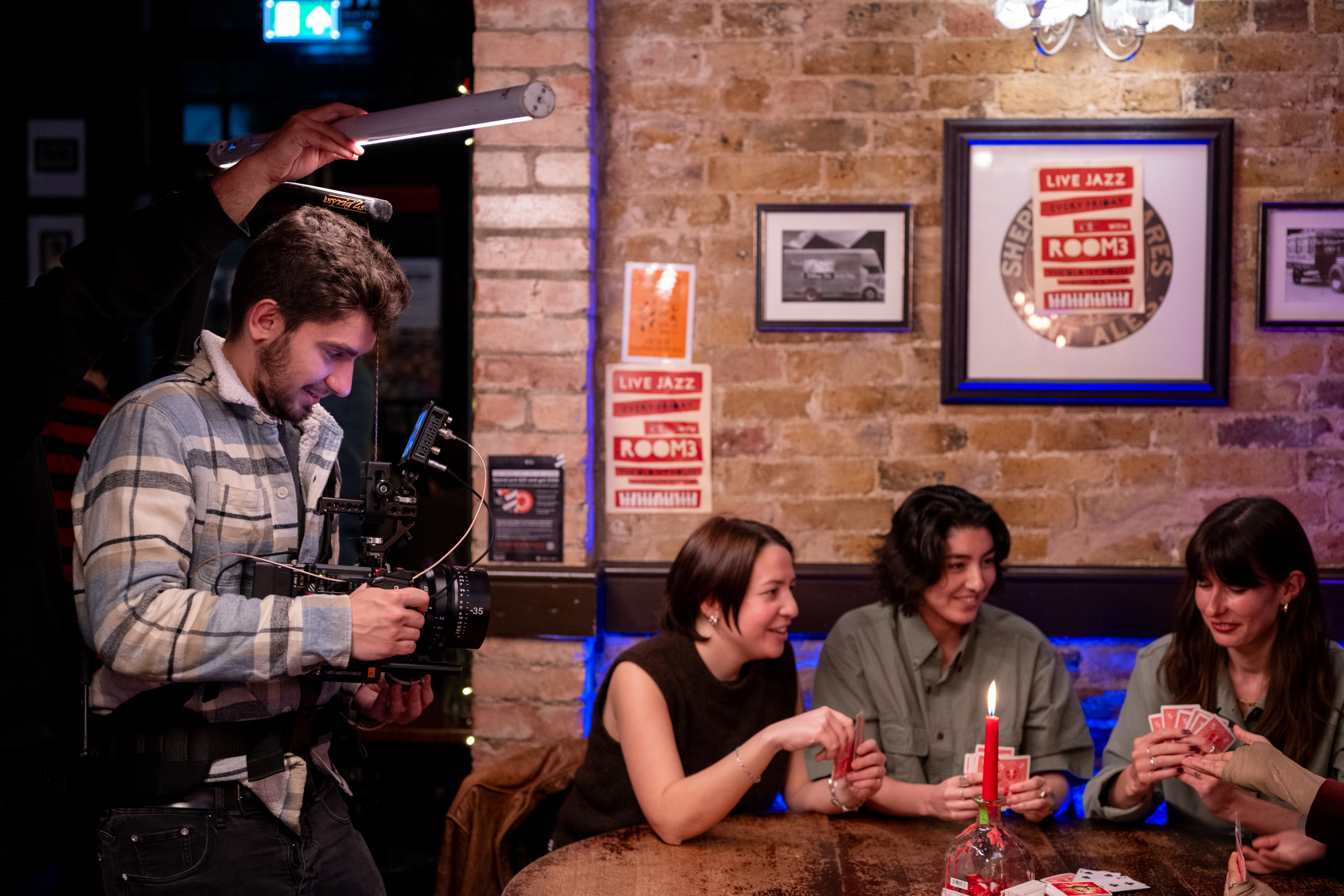 Director operating a camera beside a lit table of people during a shoot