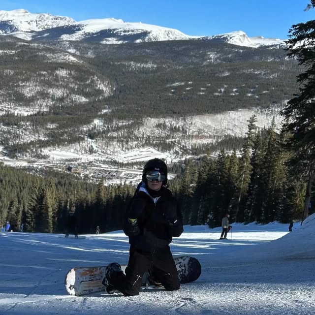 Landon seated in snowboarding gear on a snowy slope.