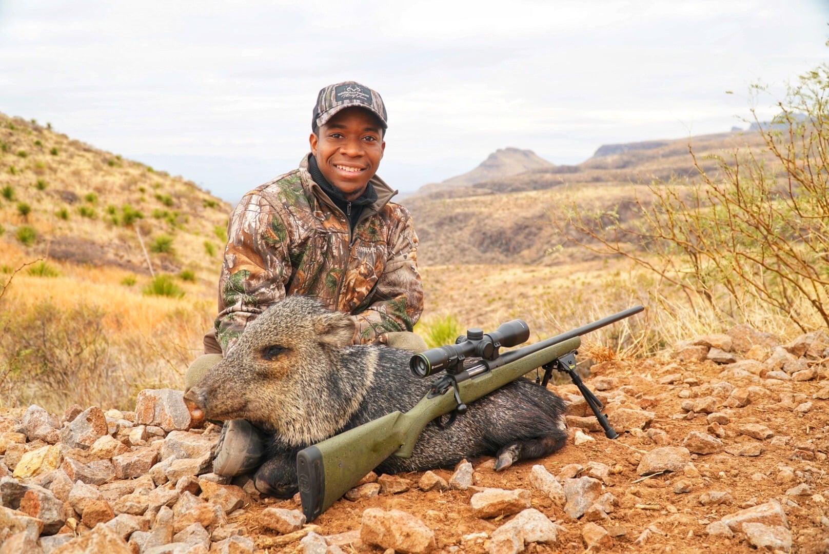 Joshua Carney with a javelina and rifle in the desert mountains