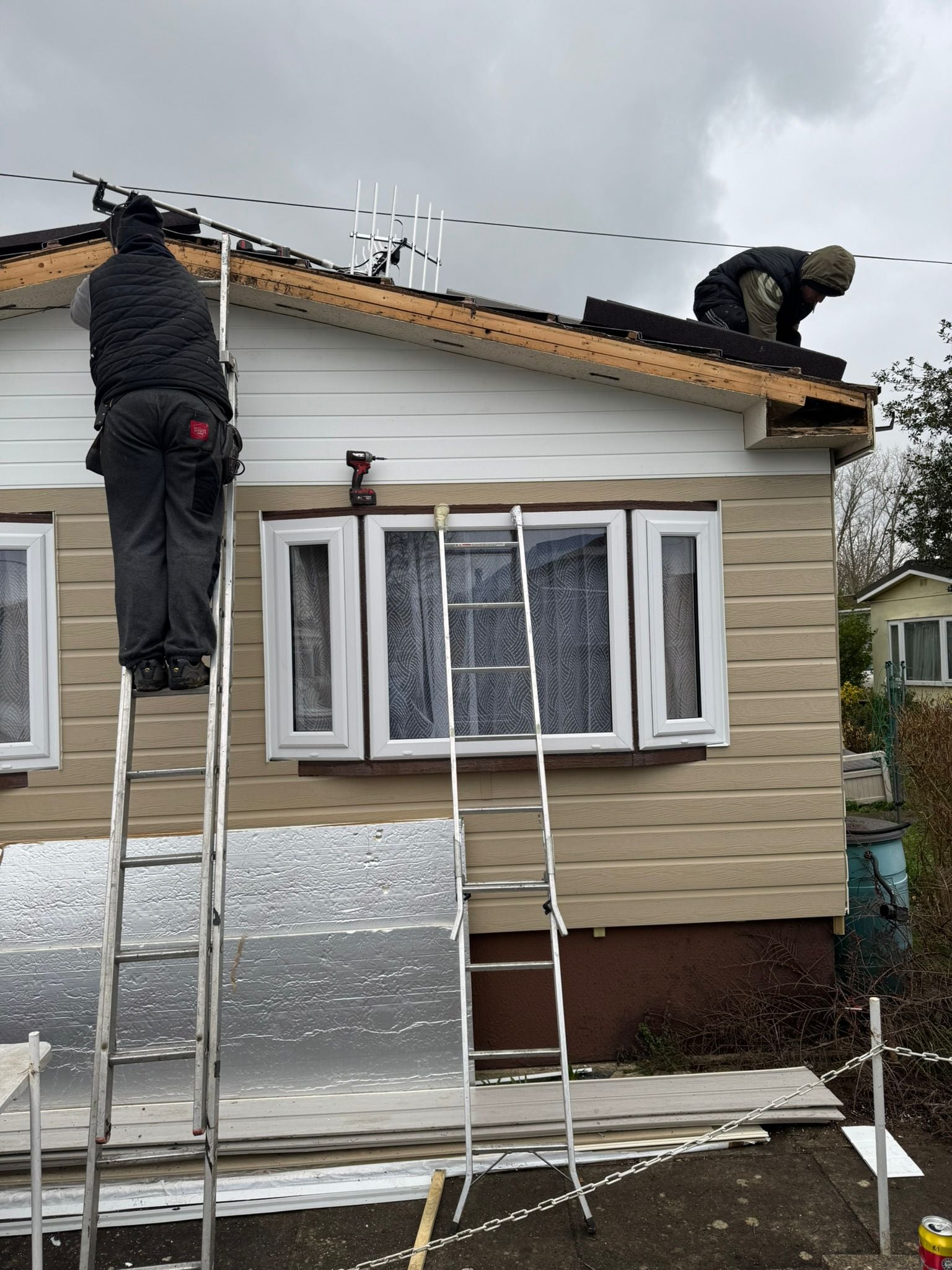 Two workers on ladders carrying out roof repair on a park home