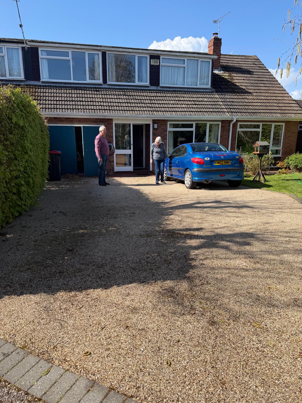 Elderly couple standing happily outside UK home on freshly cleaned driveway